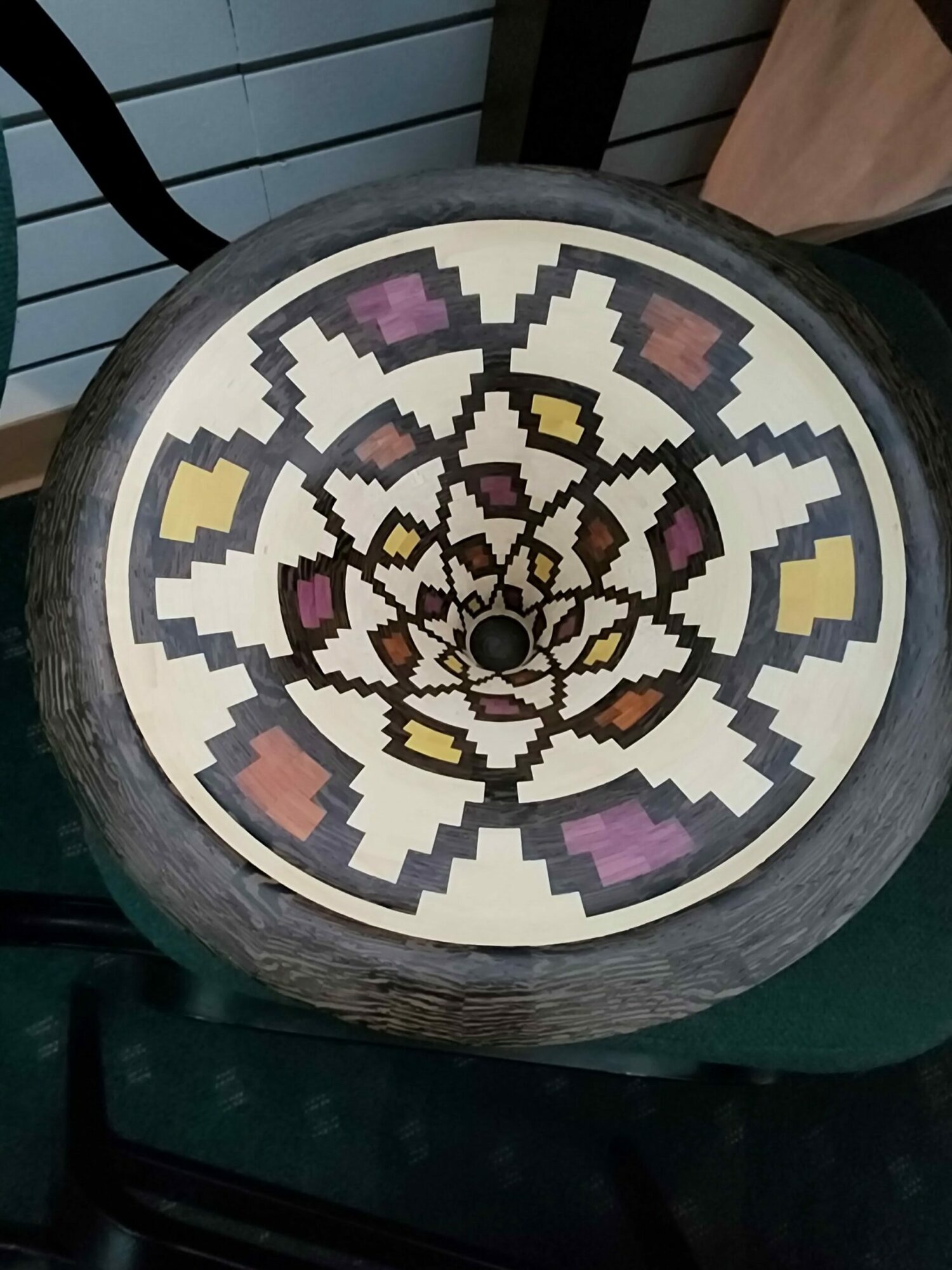 Decorative circular clock with pixelated pattern in purple, yellow, pink, and brown colors, and a dark outer rim.