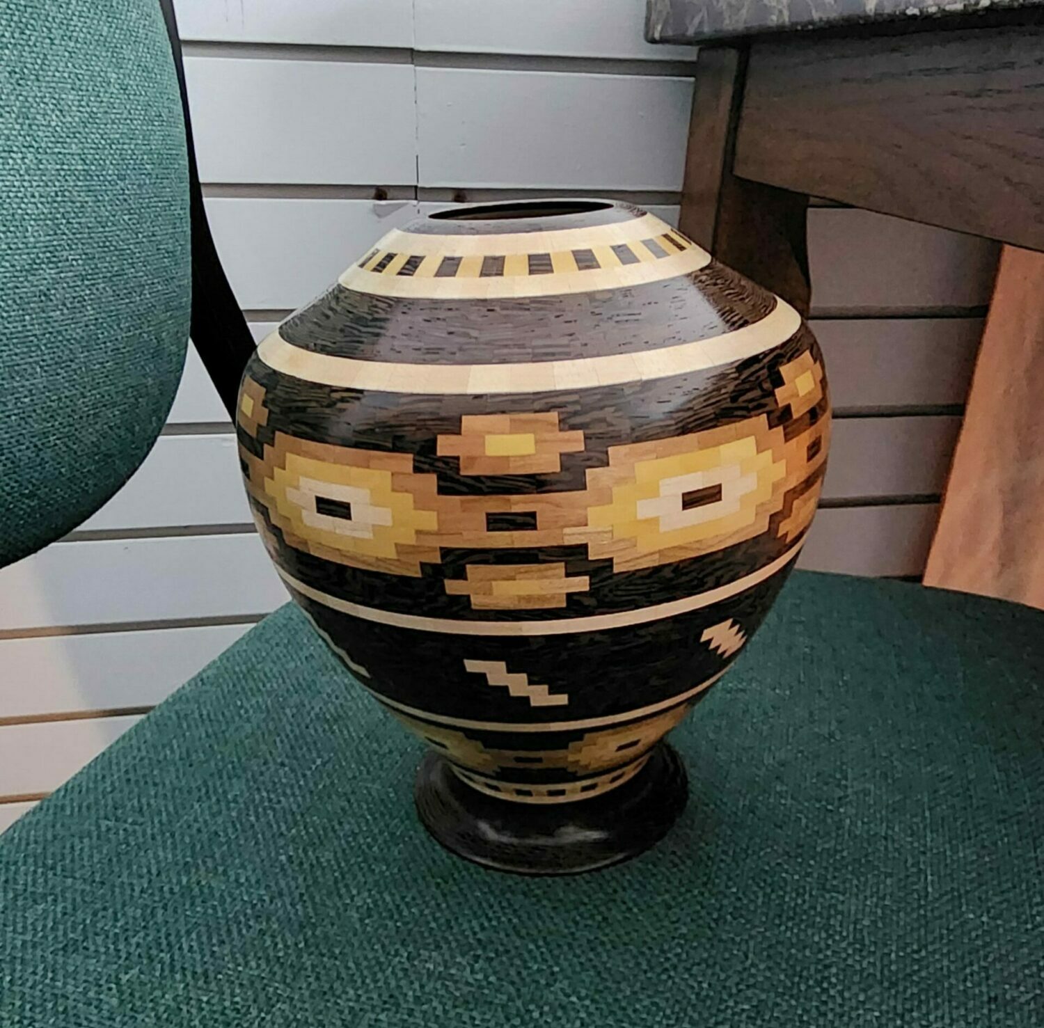 Decorative vase with geometric patterns on a green surface, with a wooden background behind it.