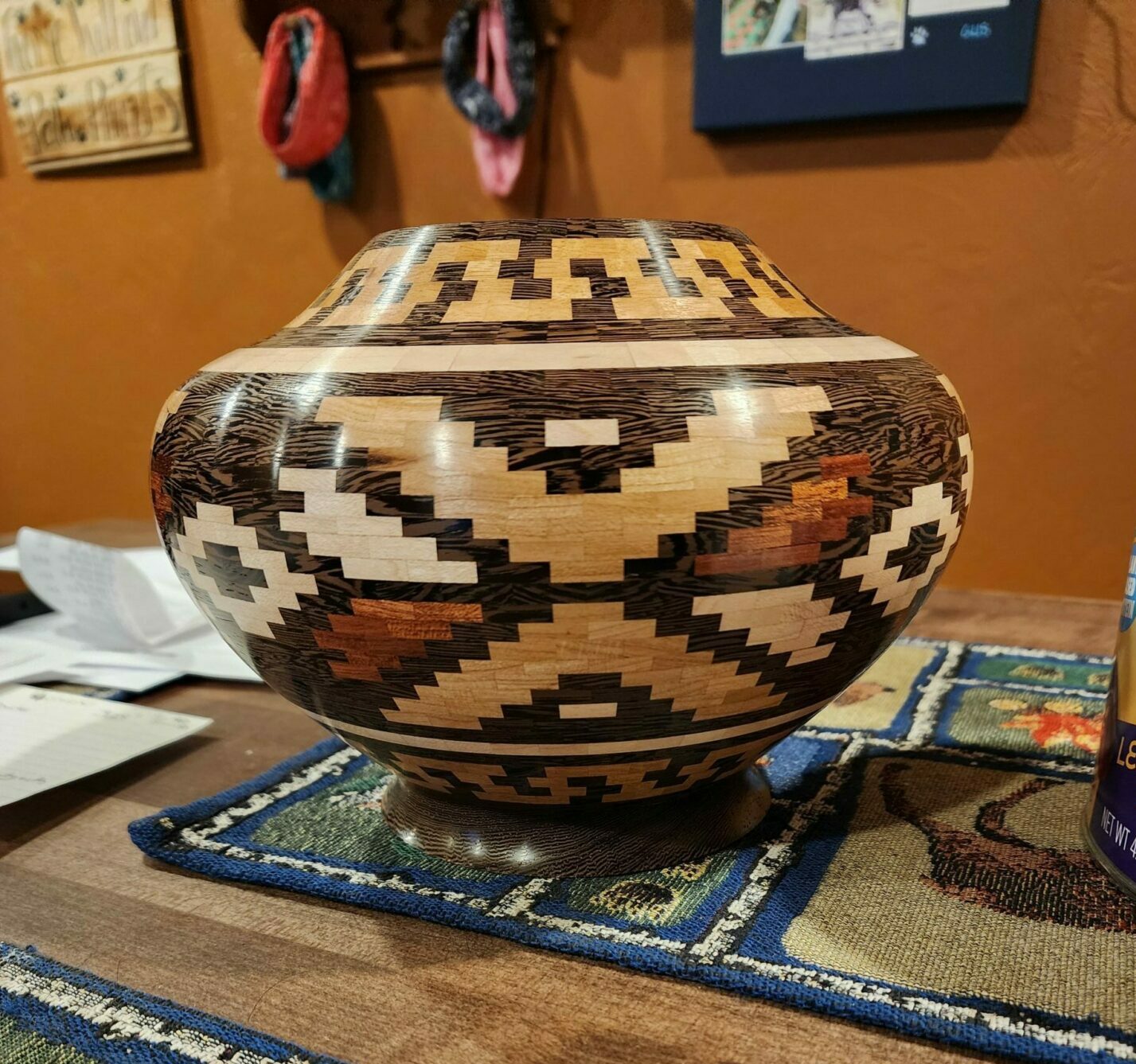 Decorative woven vase on a wooden table with a patterned rug underneath.