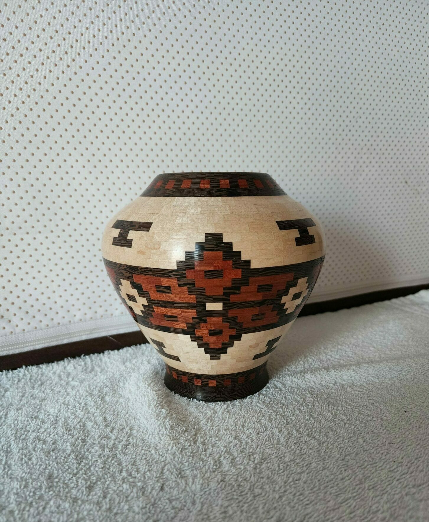 Decorative ceramic pot with geometric patterns, placed on a textured surface, with a plain background.