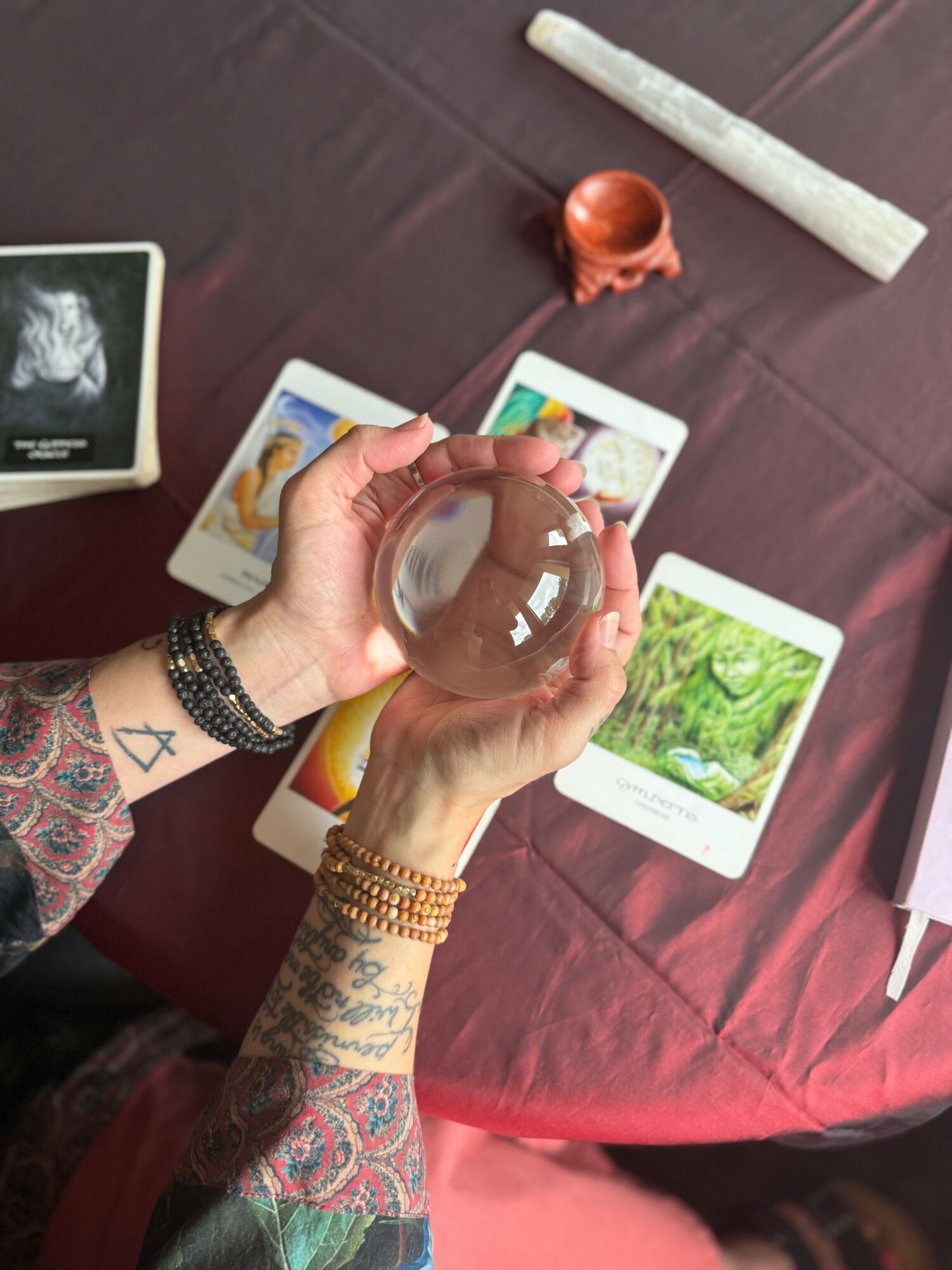 Person holding a clear crystal ball over tarot cards on a table, with a candle and a rolled scroll nearby.