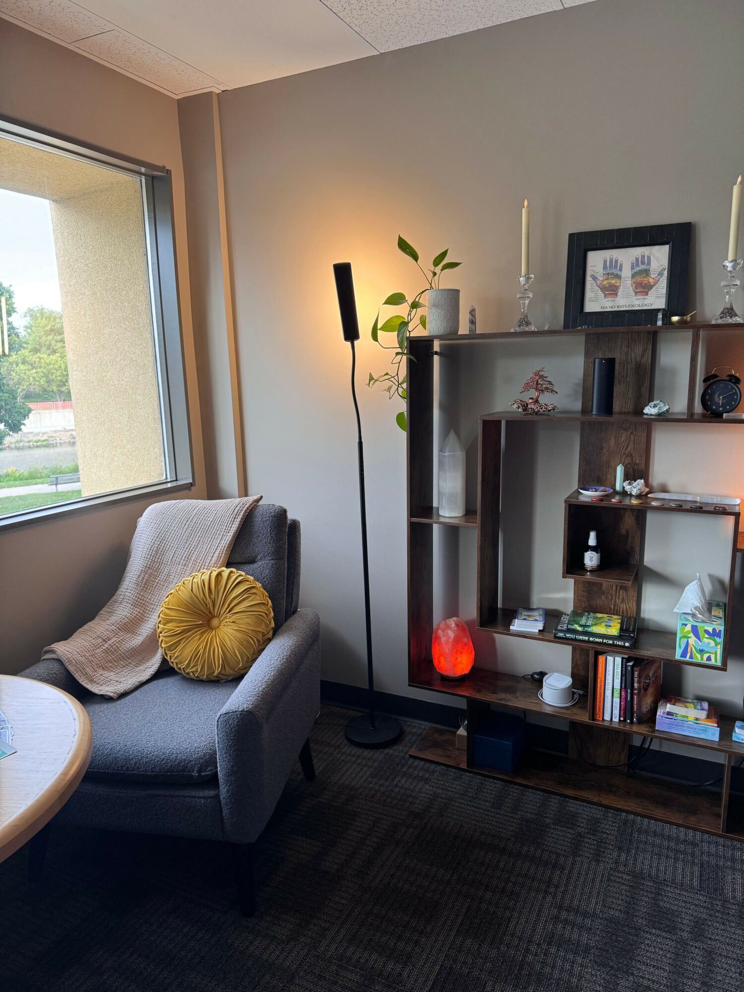 Living room with a gray armchair, yellow cushion, and a window showing outdoor greenery.