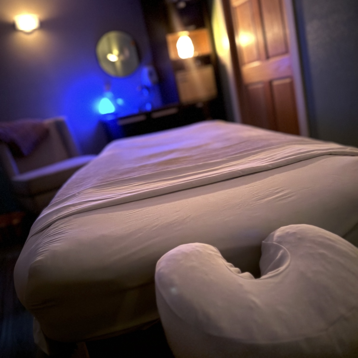 A bed with a heart-shaped pillow in a dimly lit room with colorful lights and furniture.