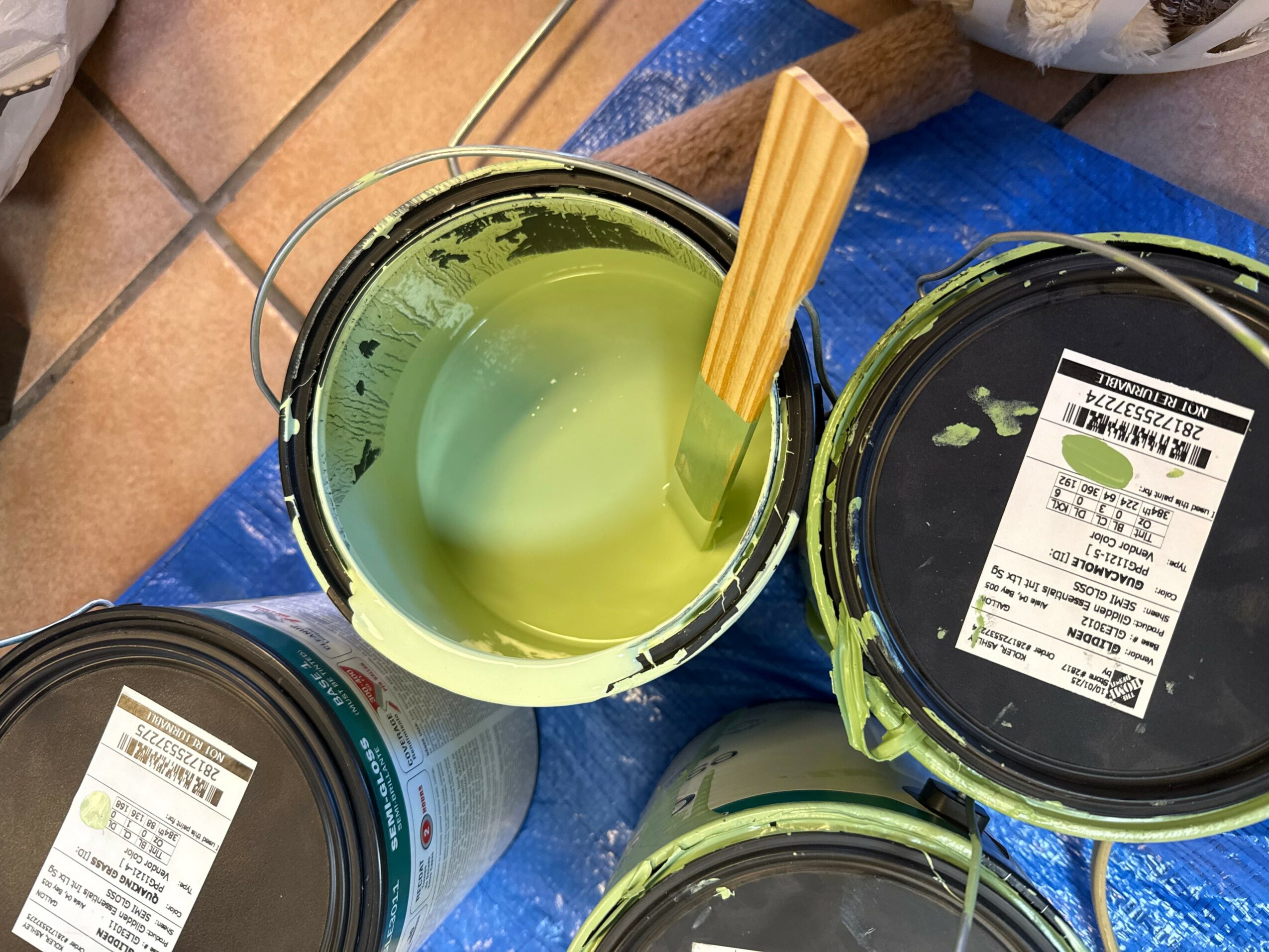 Open container with greenish liquid, a yellow stick inside, on a blue surface, with other containers nearby.