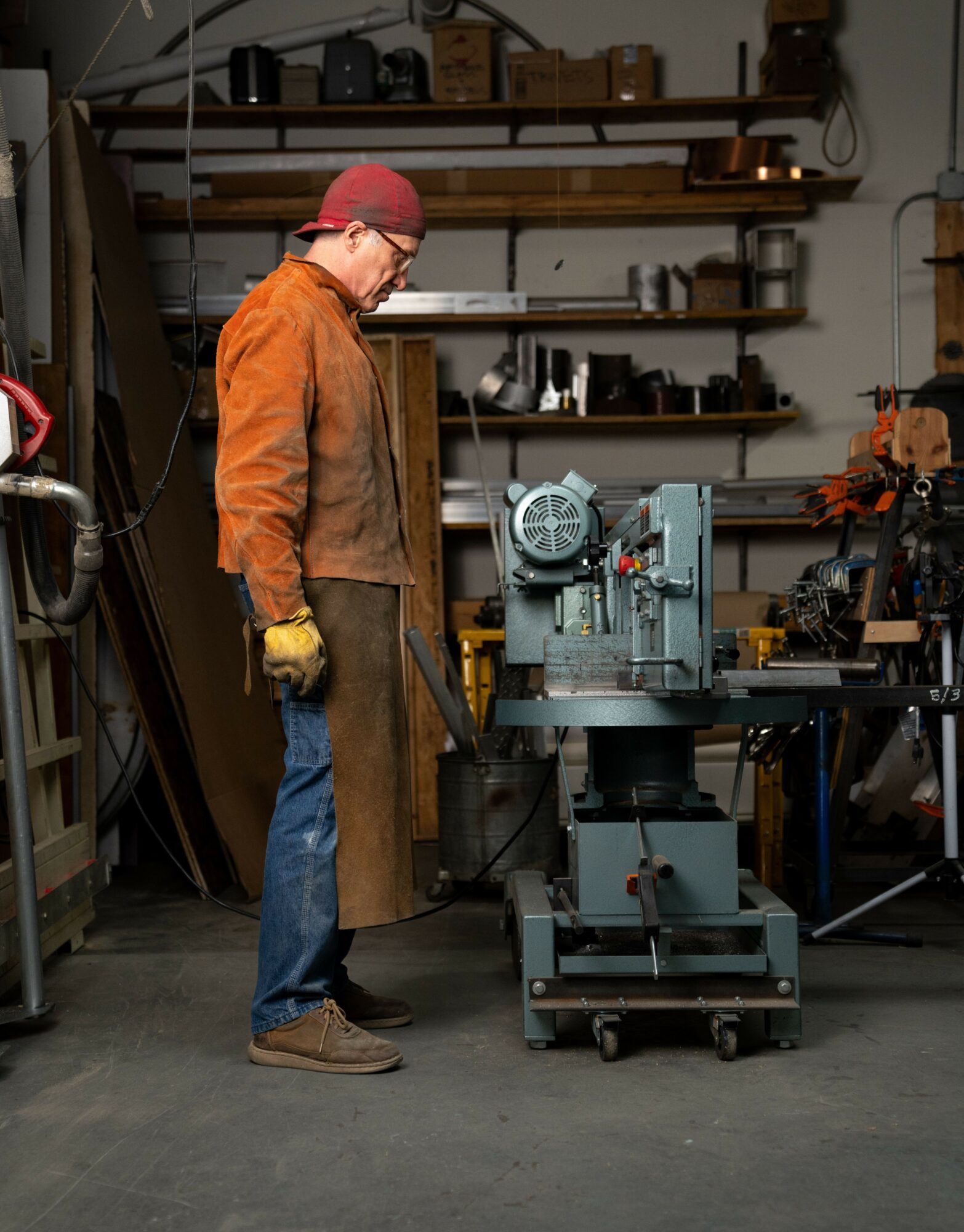 Person wearing orange jacket, red cap, and gloves working with machinery in a workshop.