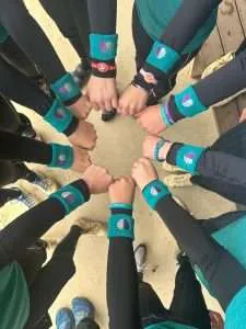 Group of people with matching blue wristbands forming a circle with fists touching in the center.