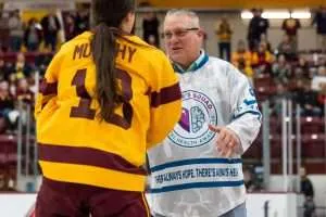 A person in a yellow and maroon sports jersey talking to a man in a white jacket inside an ice rink arena.