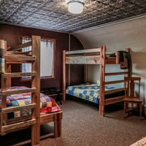 Room with wooden bunk beds, a window, a chair, and a patterned ceiling, carpeted floor, and a ceiling light.