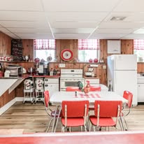 Kitchen with wooden walls, white appliances, a dining table with red chairs, and a clock on the wall.