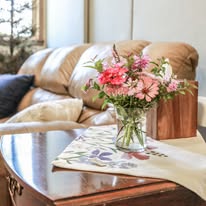 Vase with pink flowers on a table in a cozy living room with a sofa and cushions.