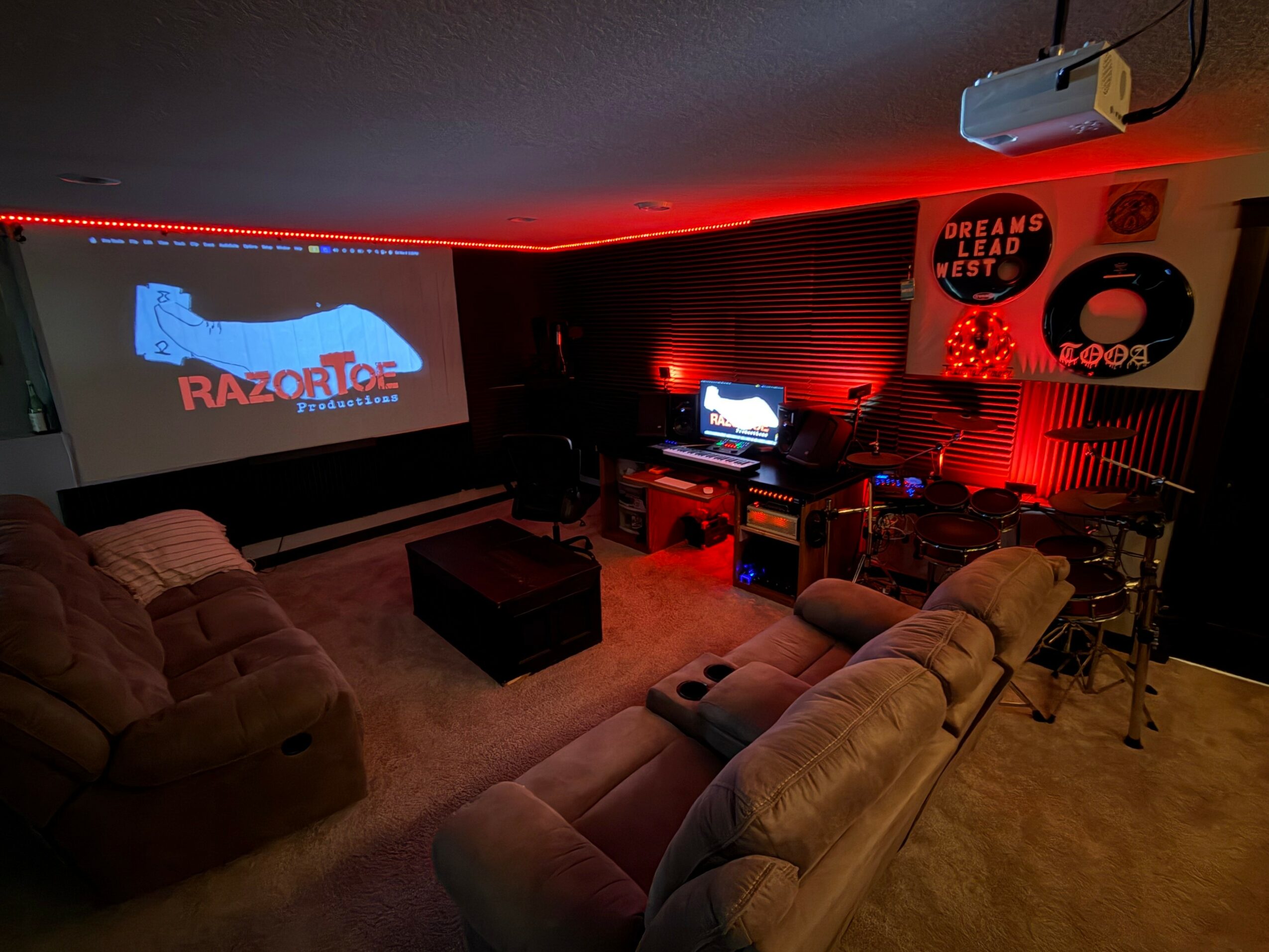 Home theater room with large beige sectional sofa, projector screen, and gaming setup illuminated by red lighting.