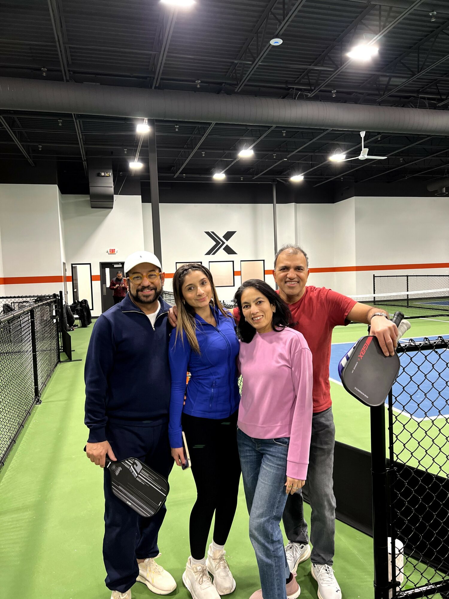 Four people standing together inside a sports facility, smiling, with a boxing ring in the background.