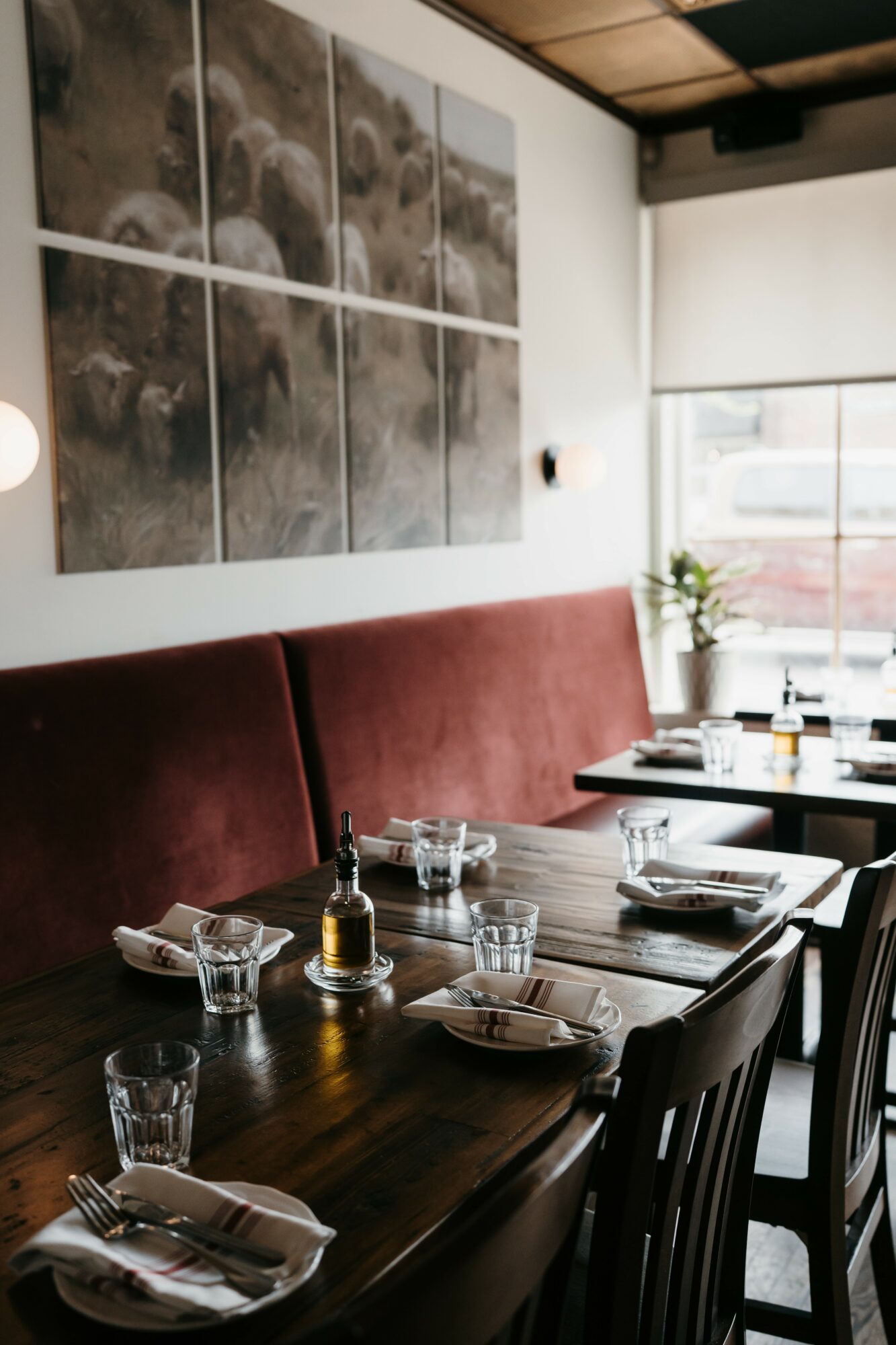 Dining table set with glasses, plates, and napkins in a restaurant with a red bench and artwork on the wall.