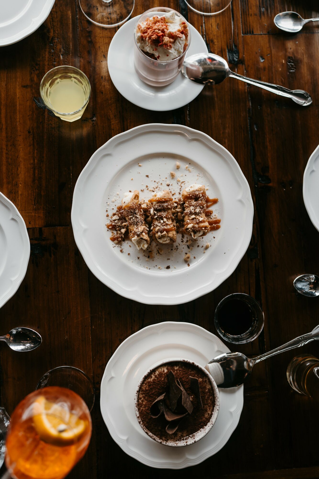 Dessert table with cake, coffee, and drinks on white plates and glasses, viewed from above.