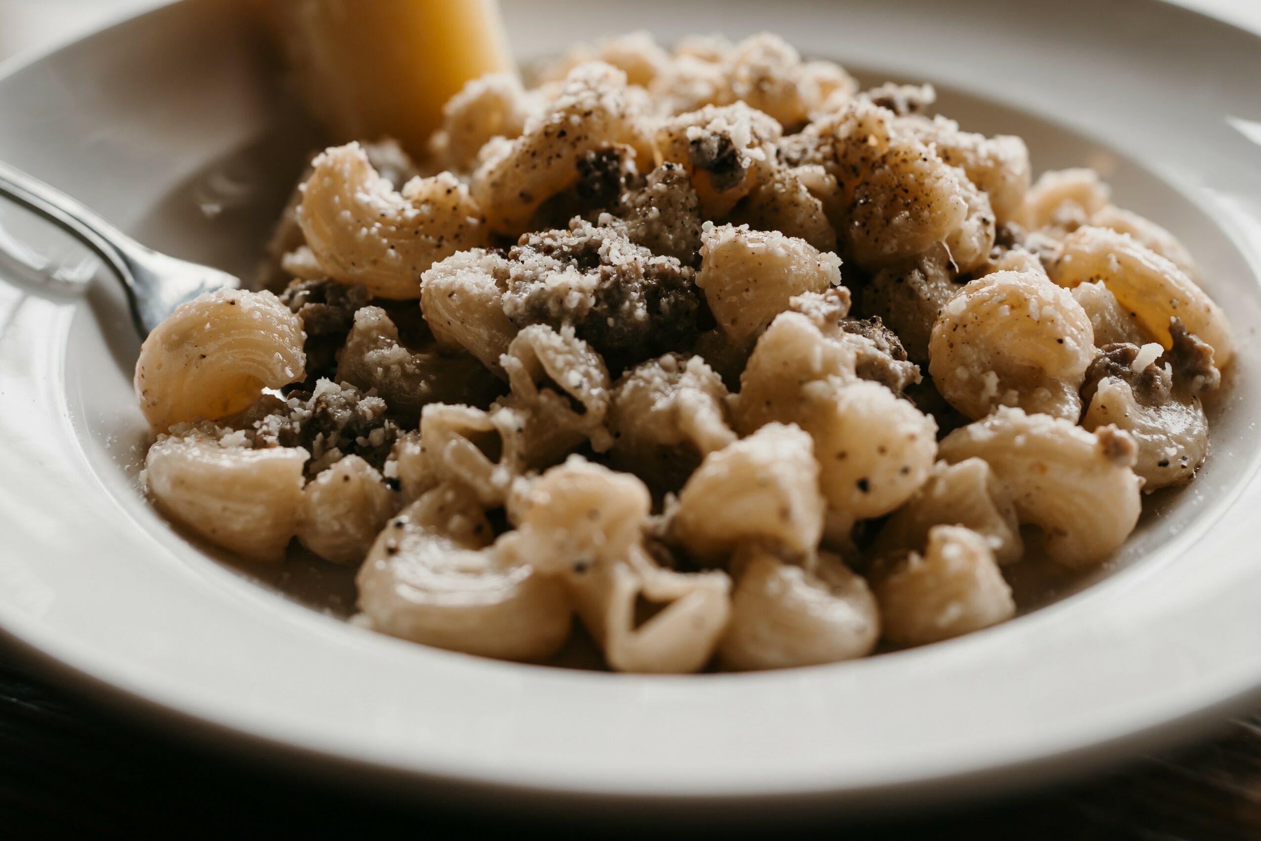 Plate of gnocchi with grated cheese, fork on the side, close-up view, in a white bowl.