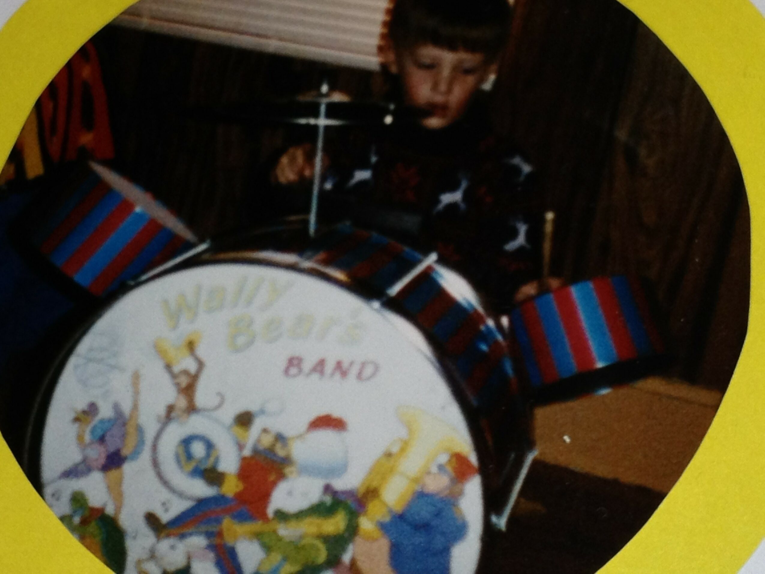 Child playing with a drum decorated with cartoon characters and the words 'Wally Bear BAND'.