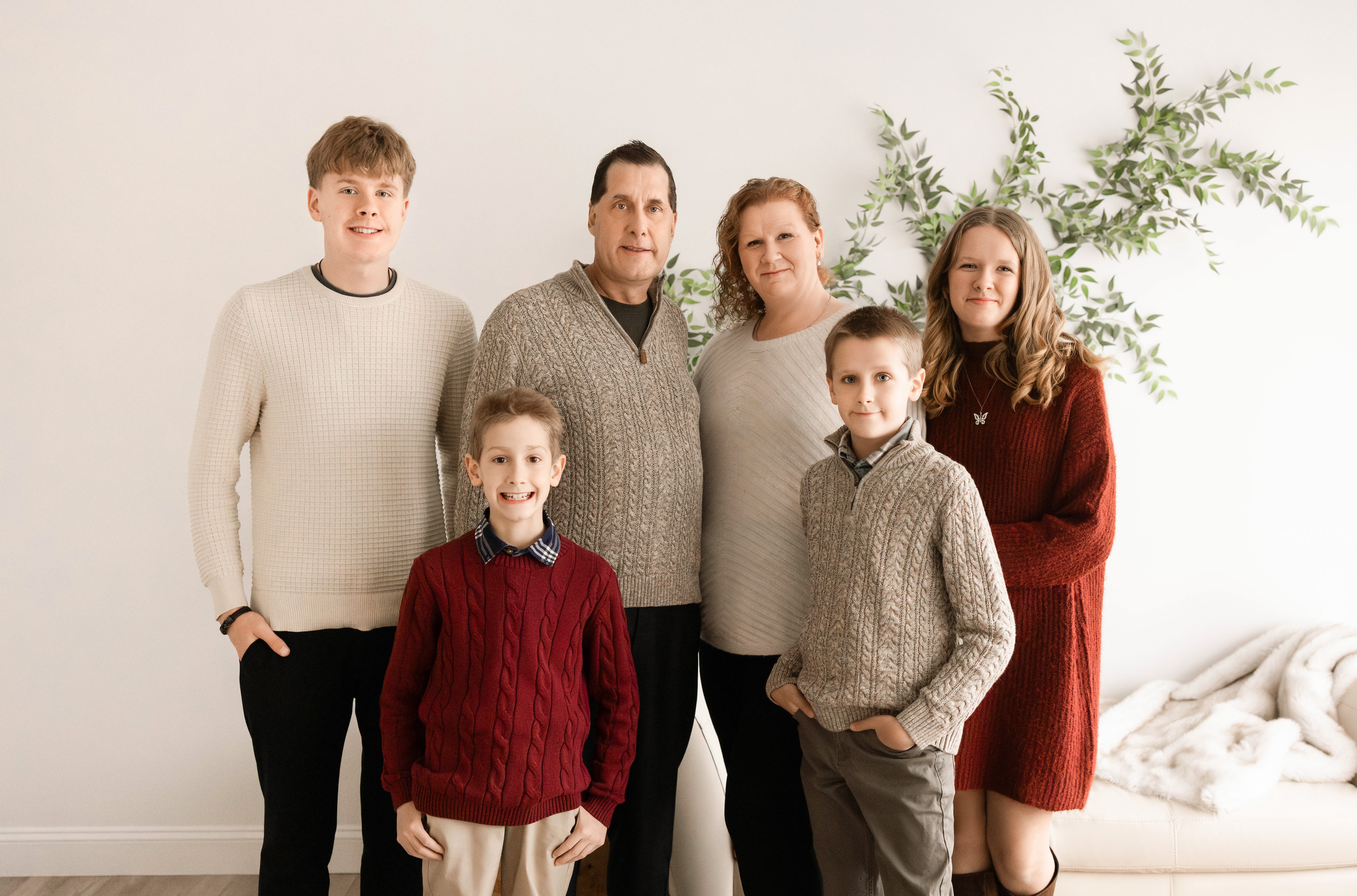 Group of six people standing indoors with a plant in the background, smiling, in casual clothing.