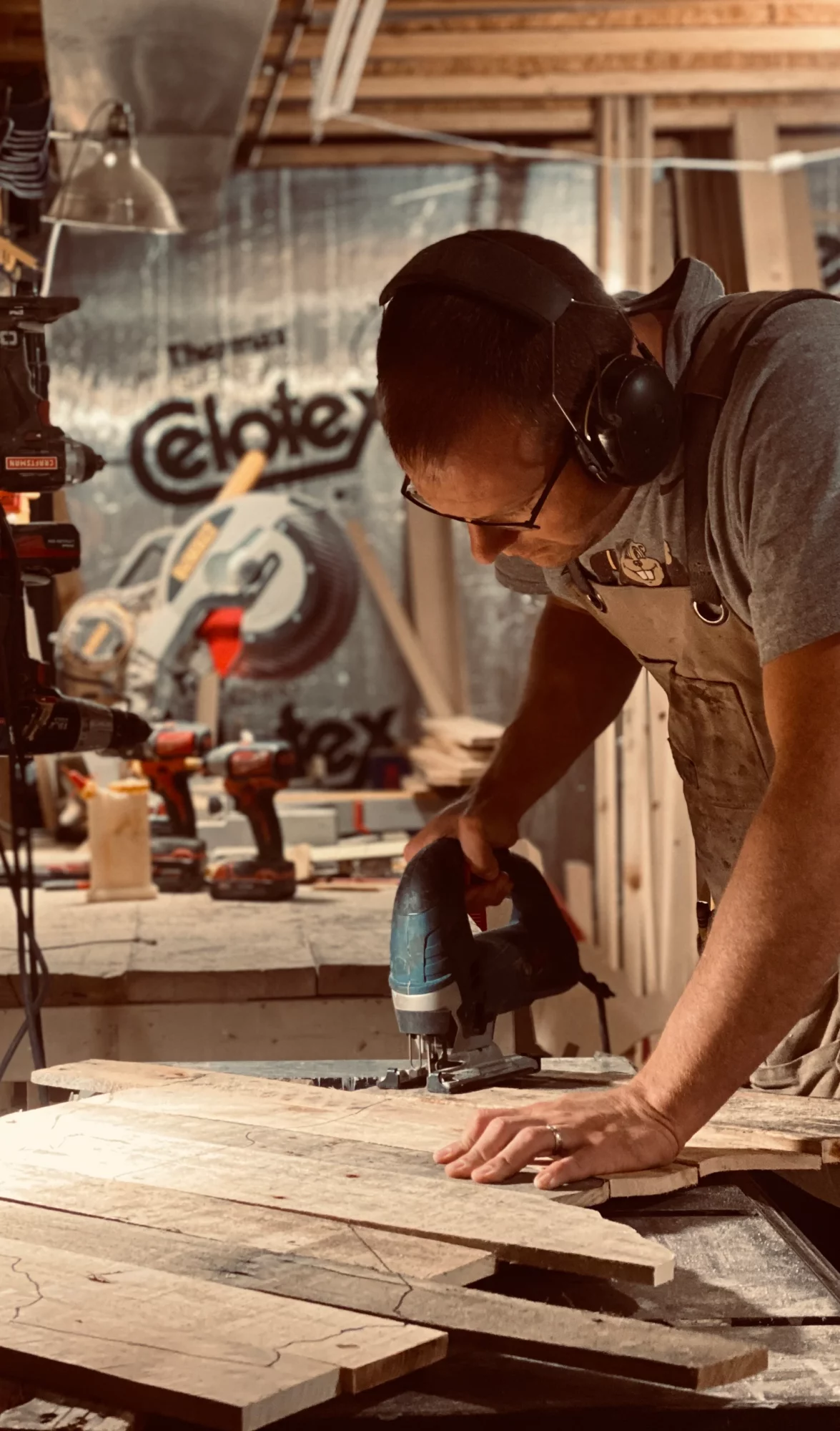 Person working with a power tool on a wooden surface in a workshop, wearing safety glasses and headphones.