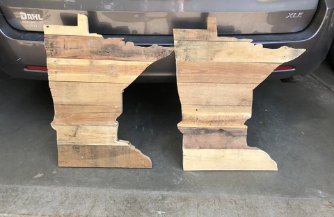 Two wooden cutouts resembling the shape of a person, placed on a concrete surface in front of a vehicle.