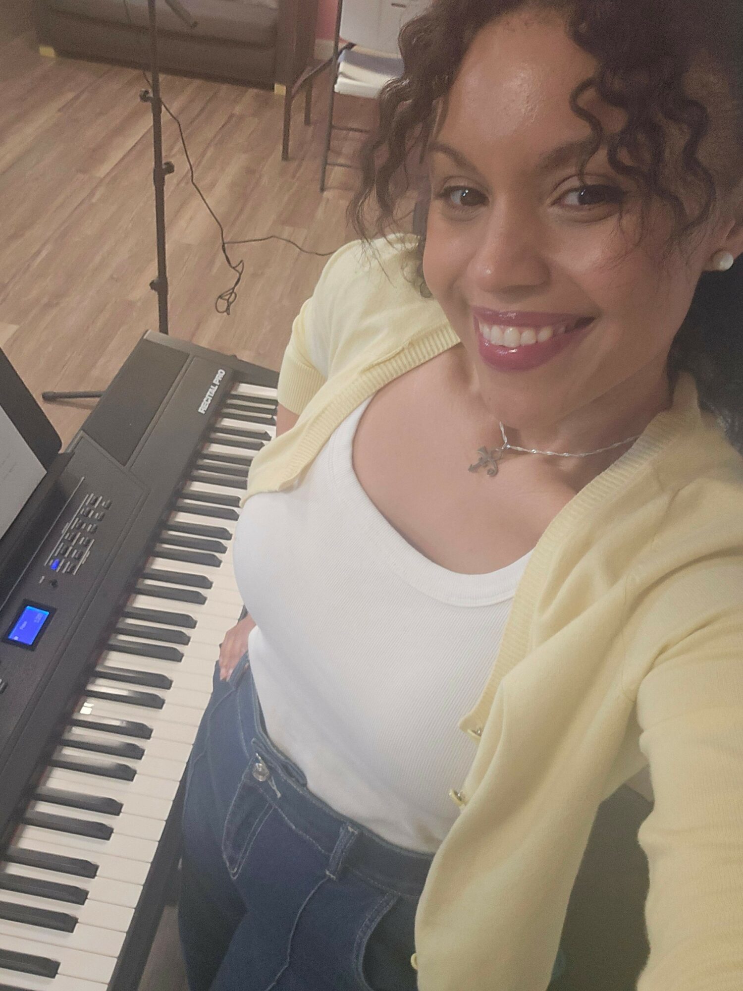 Woman with curly hair smiling, lying next to a keyboard, wearing a white top and yellow jacket.
