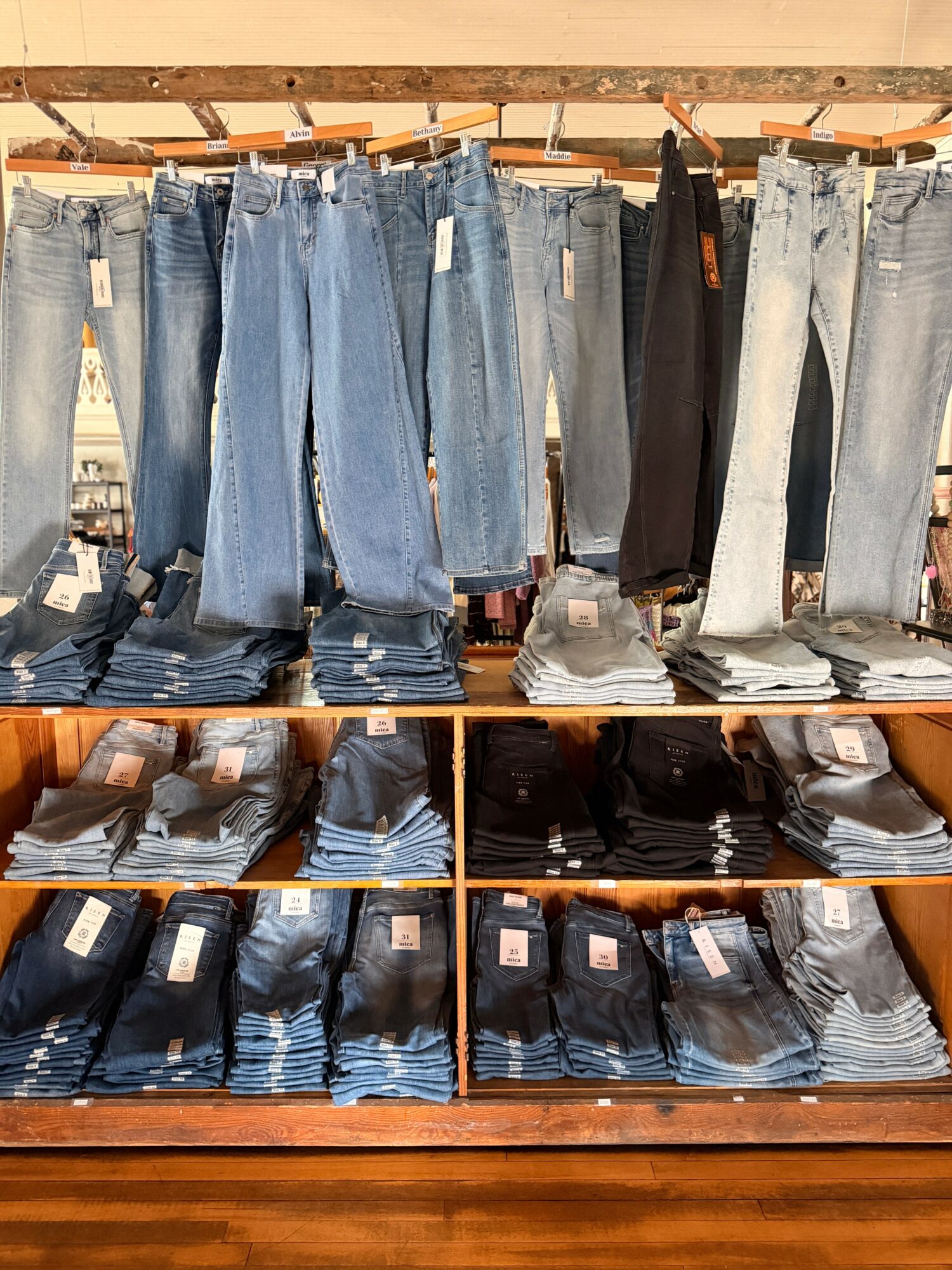 Display of various jeans hanging on a rack and folded on shelves below, in a store setting.