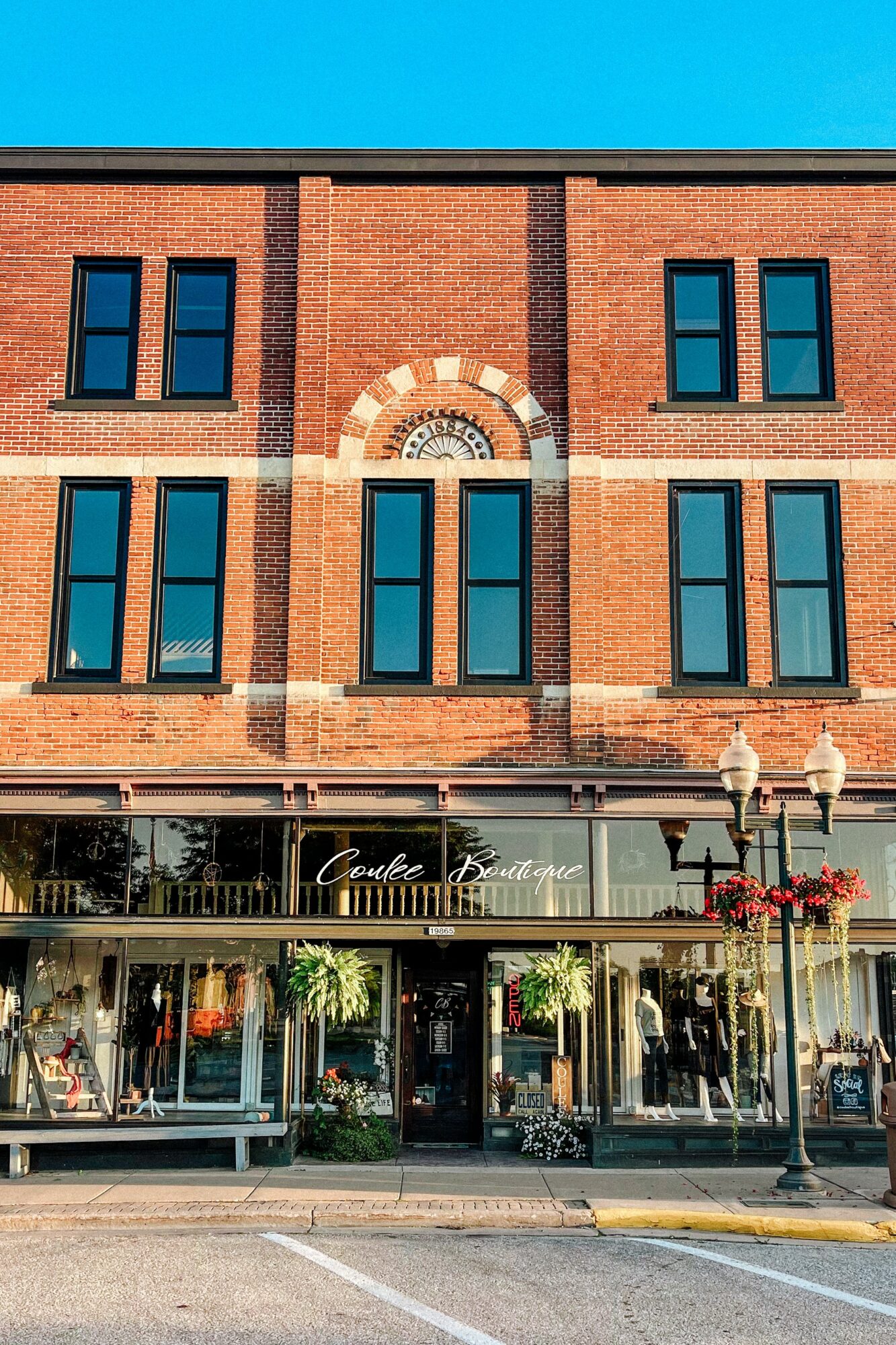 Brick building with large windows and a storefront on the ground level, decorated with plants and flowers.