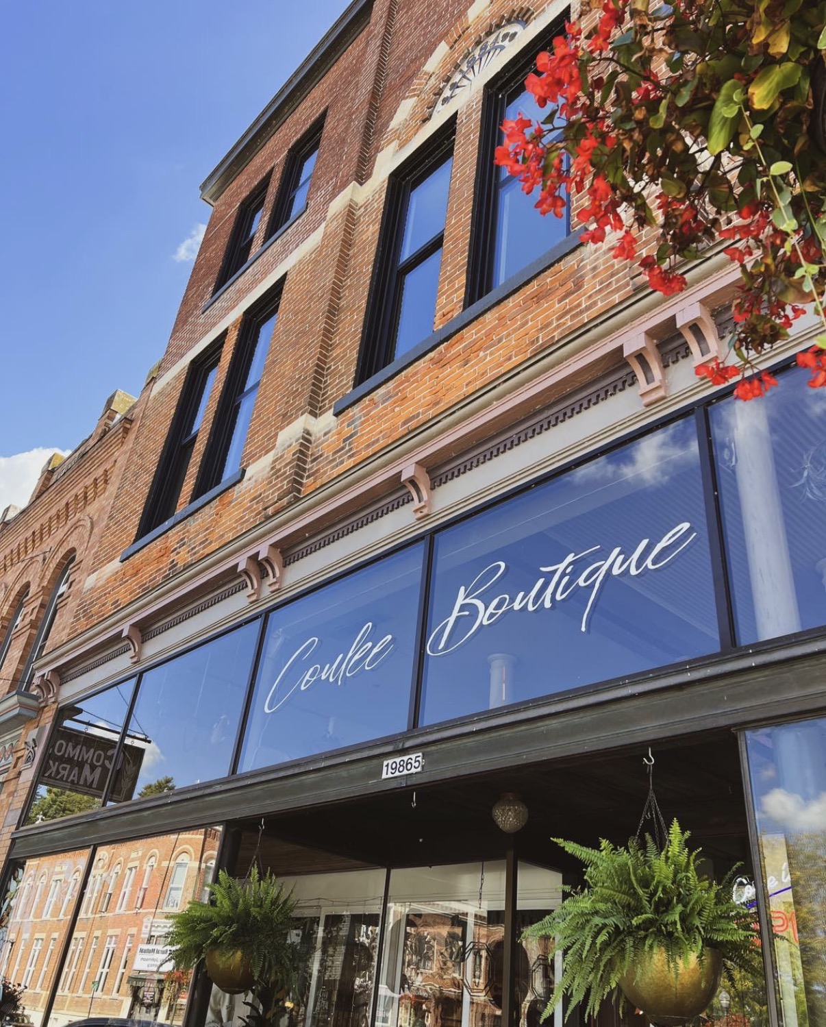 Storefront with a sign reading 'Candle Boutique' on a brick building, with hanging plants and a clear sky.