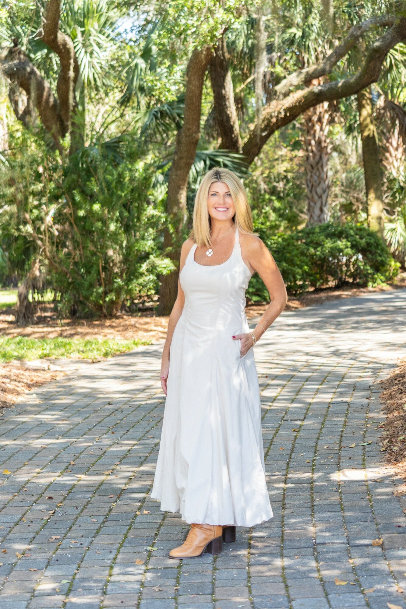 Woman in white dress standing on paved path in park with trees and greenery in background