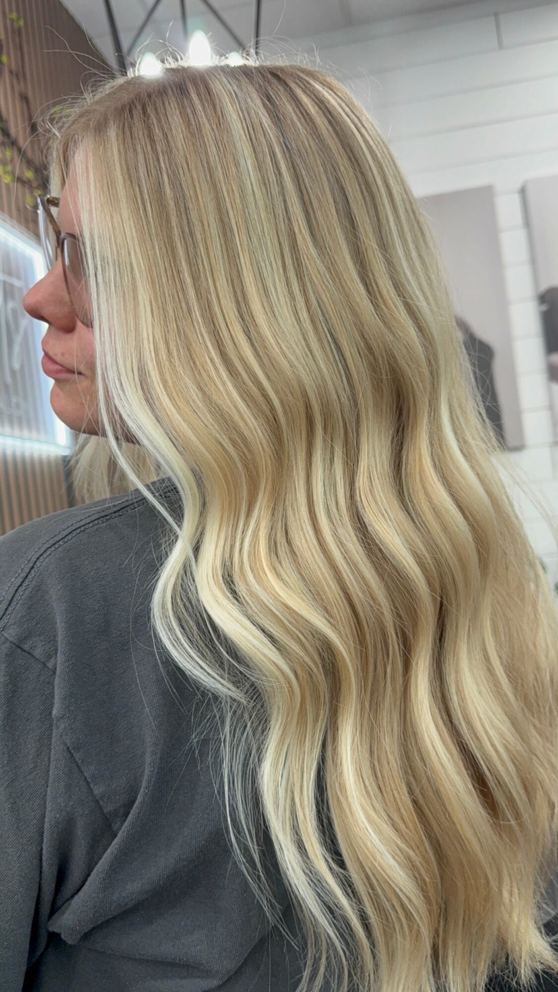 Side view of a woman with long, wavy blonde hair in an indoor setting.