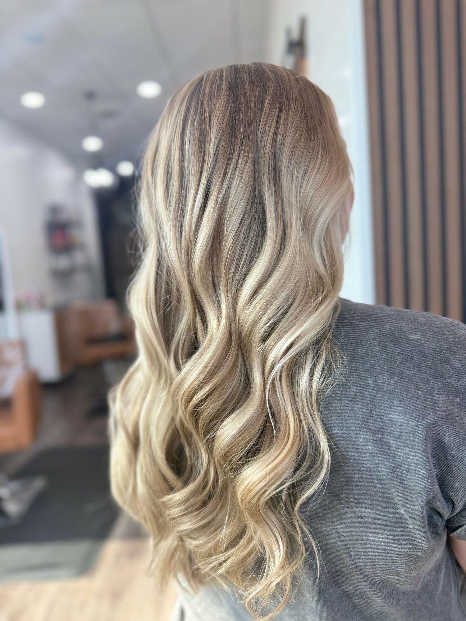 Back view of a woman with long, wavy, blonde hair in a salon setting.