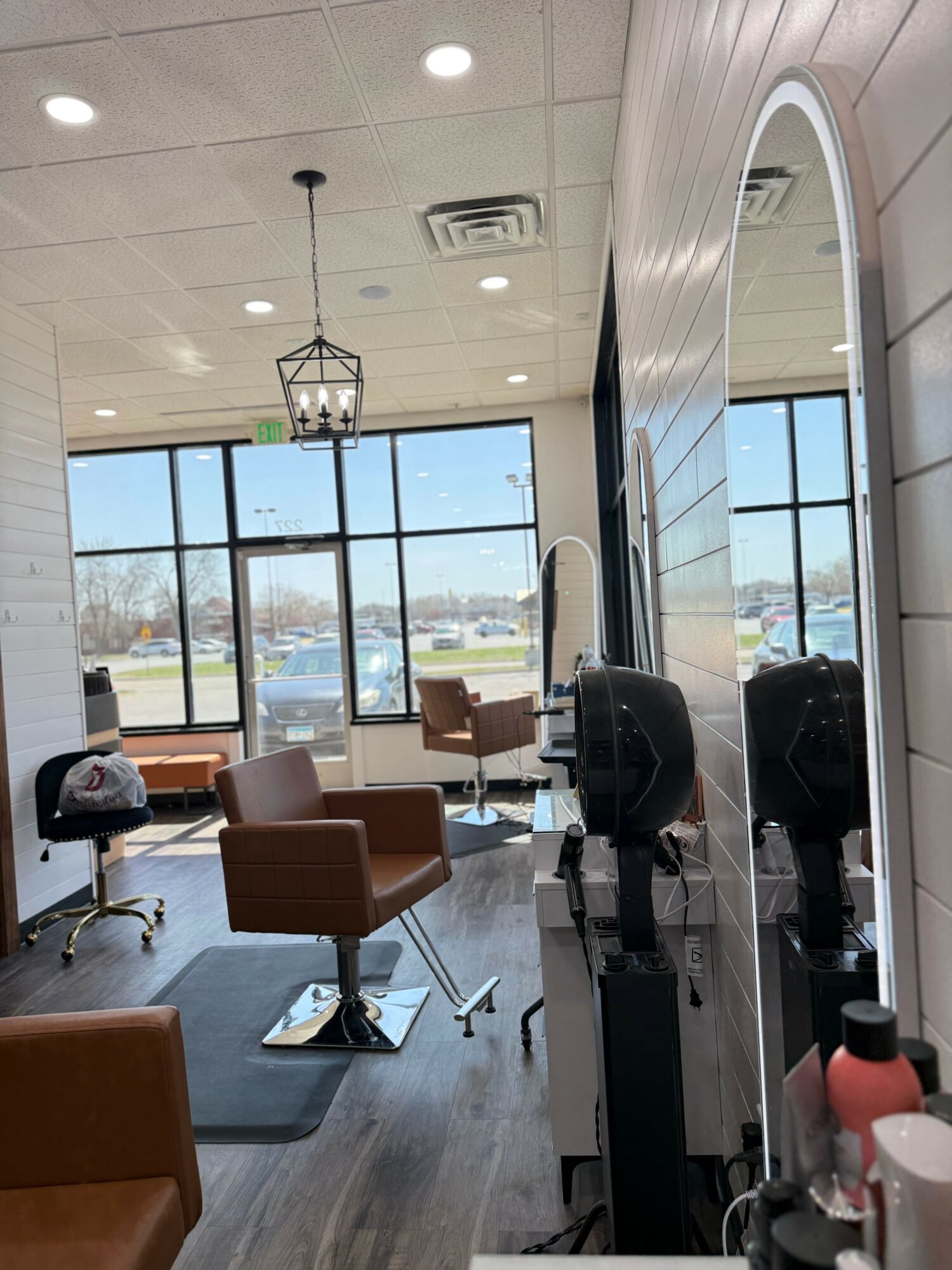 Salon interior with chairs, large windows, and a mirror, showing a parking lot outside.