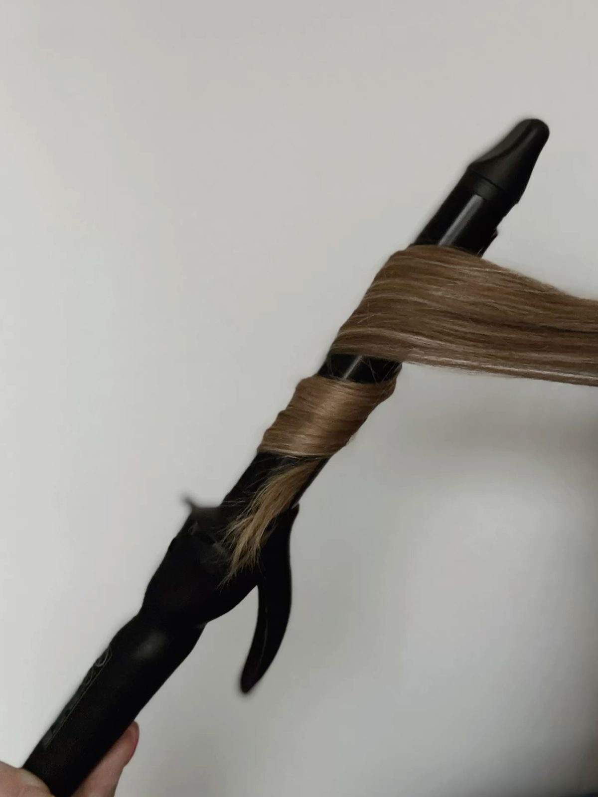 A curling iron with a section of hair wrapped around it, held against a plain white background.