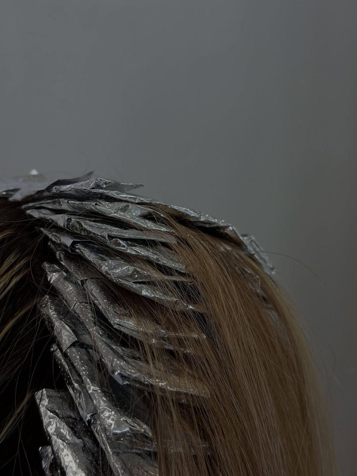 Close-up of a person's head with hair and hair rollers wrapped in foil, against a plain background.