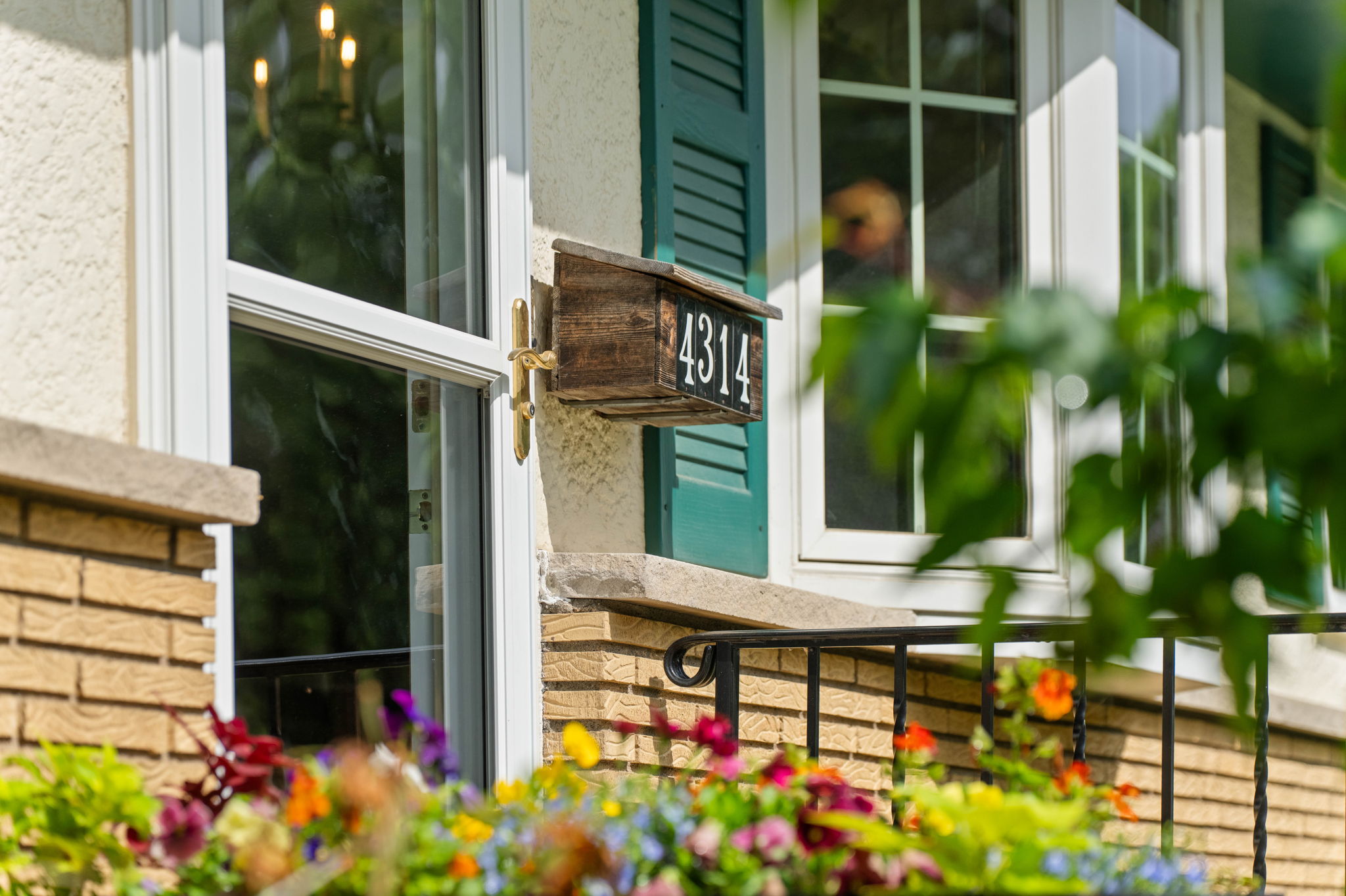 Close-up of a house exterior with a wooden mailbox displaying the number 4312, surrounded by colorful flowers and greenery.