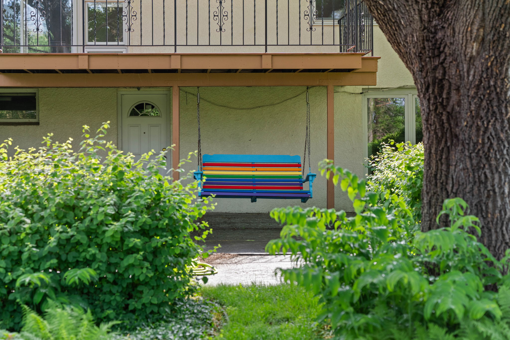 Colorful striped swing seat hanging between two trees in a garden, with a house in the background.