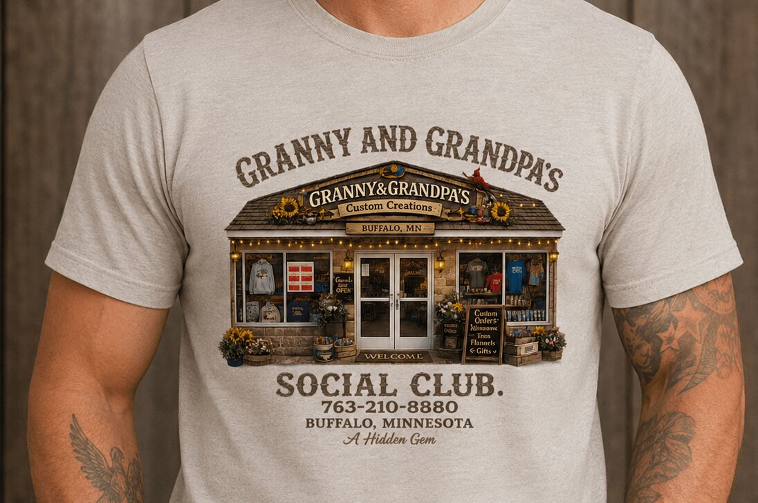 Person wearing a light-colored T-shirt with a graphic and text about a social club, tattoo visible on arm.