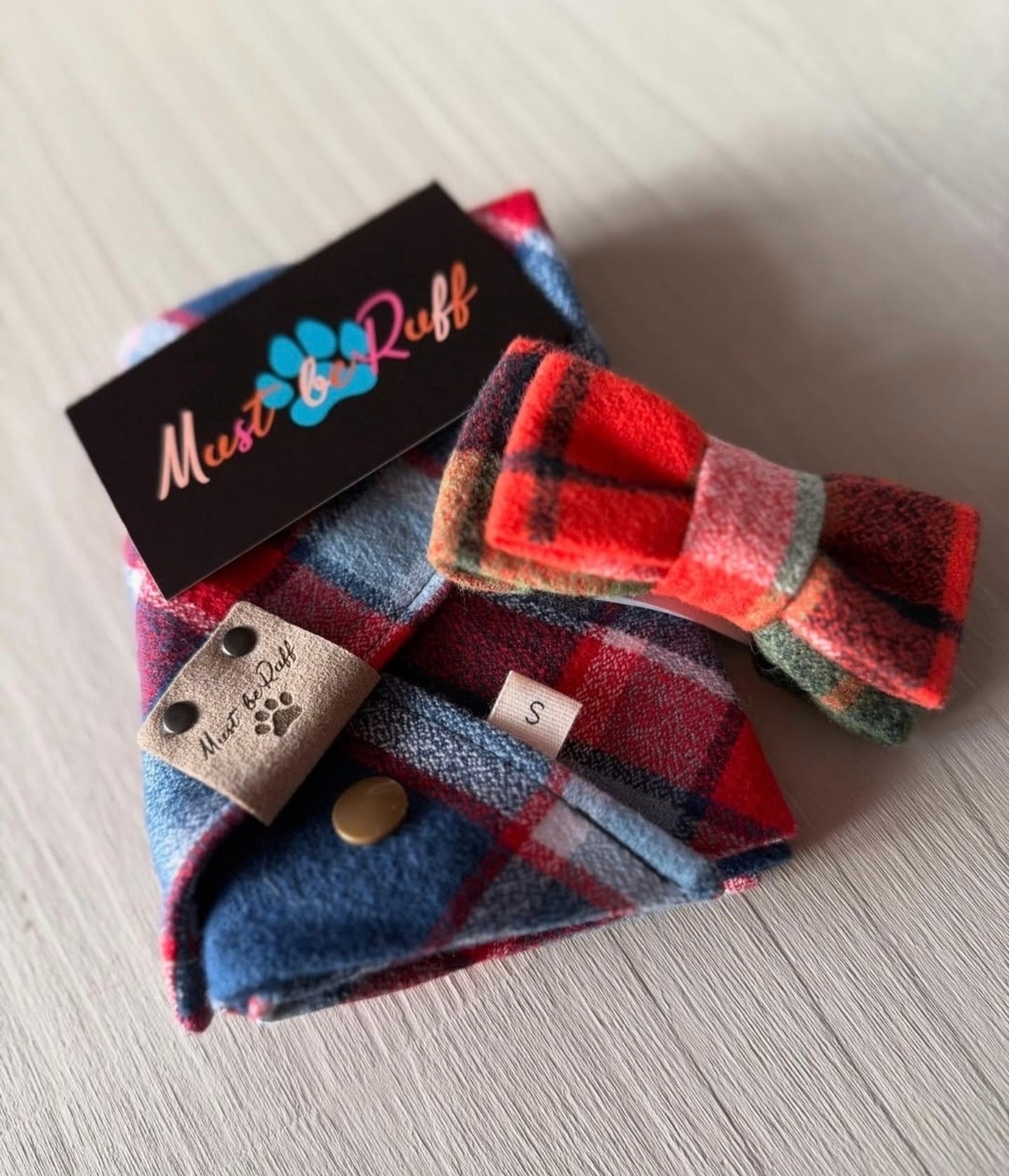 Folded plaid fabric with a bow, a tag, and a small label, on a light surface.