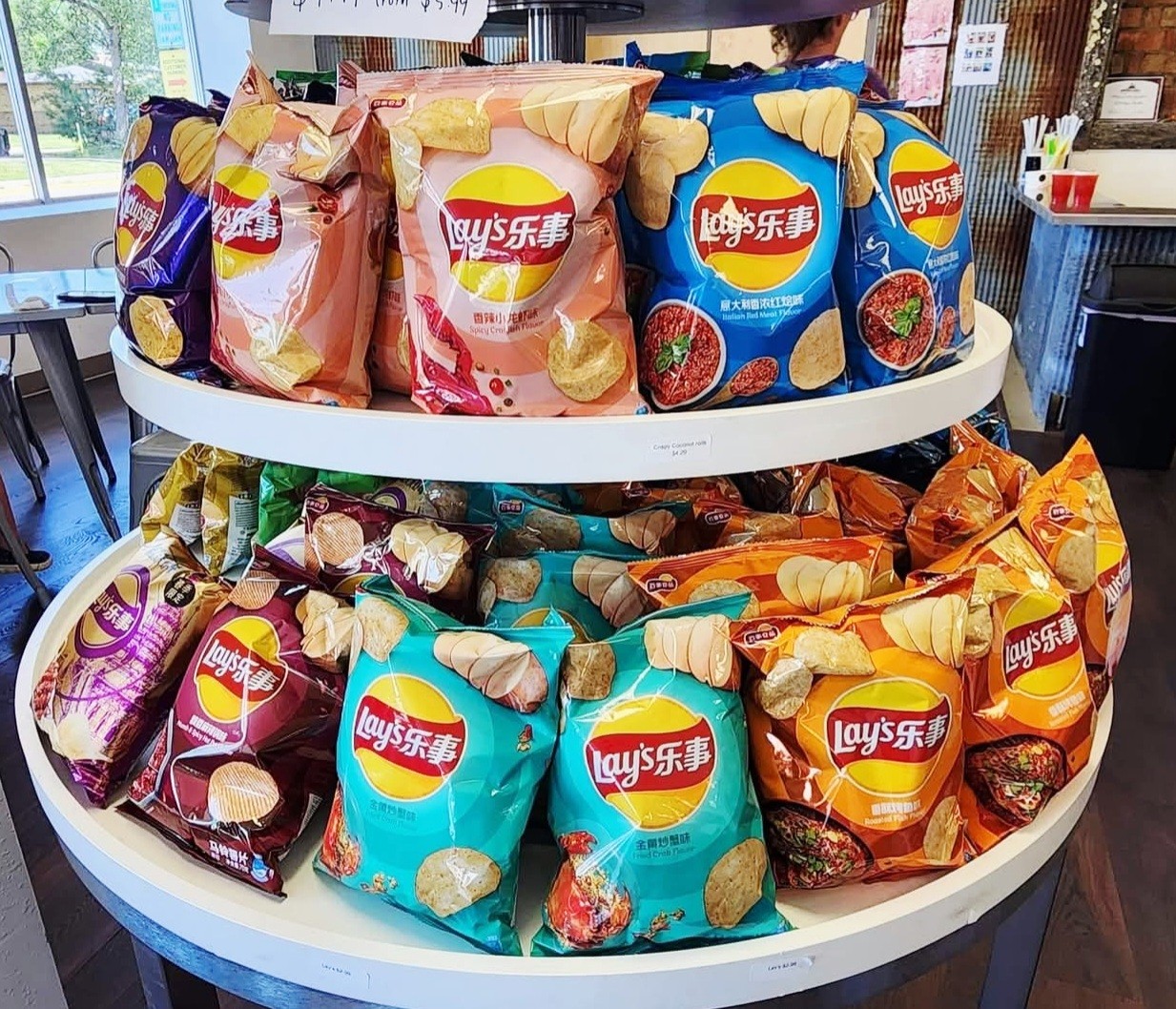 Two-tier display of Lay's potato chip bags in various flavors and colors on a round table inside a store.