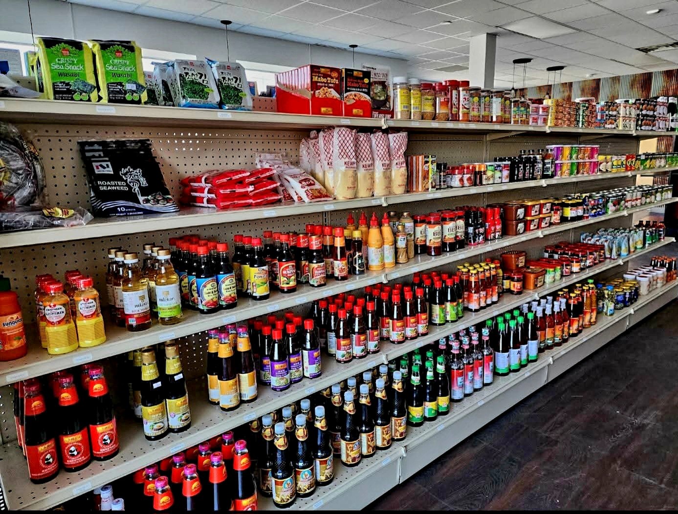 Store shelf stocked with various bottles, jars, and packages of condiments and sauces, organized in rows.
