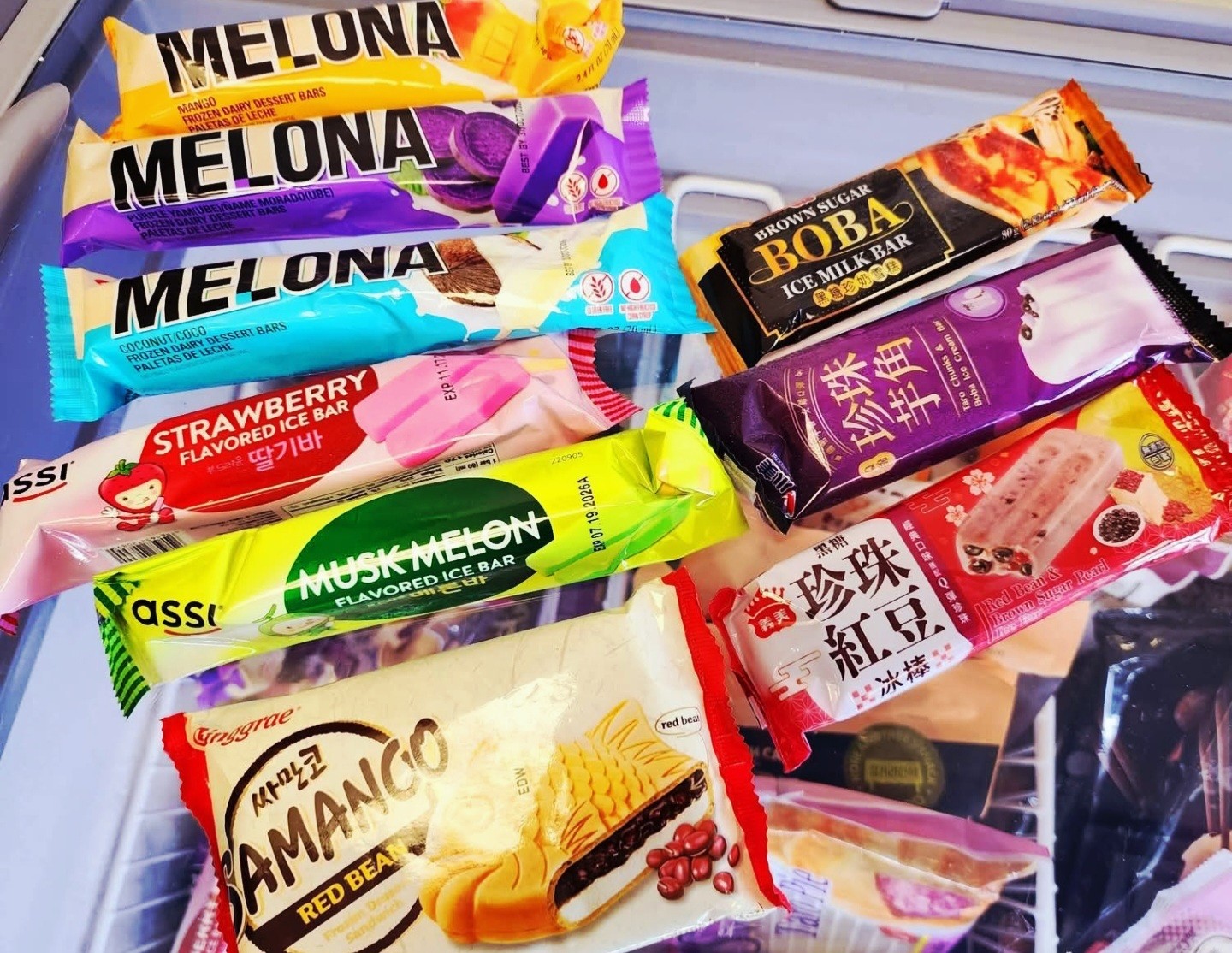 Assorted snack bars and cookies in colorful packaging on a surface, including Melona, strawberry, and other flavors.