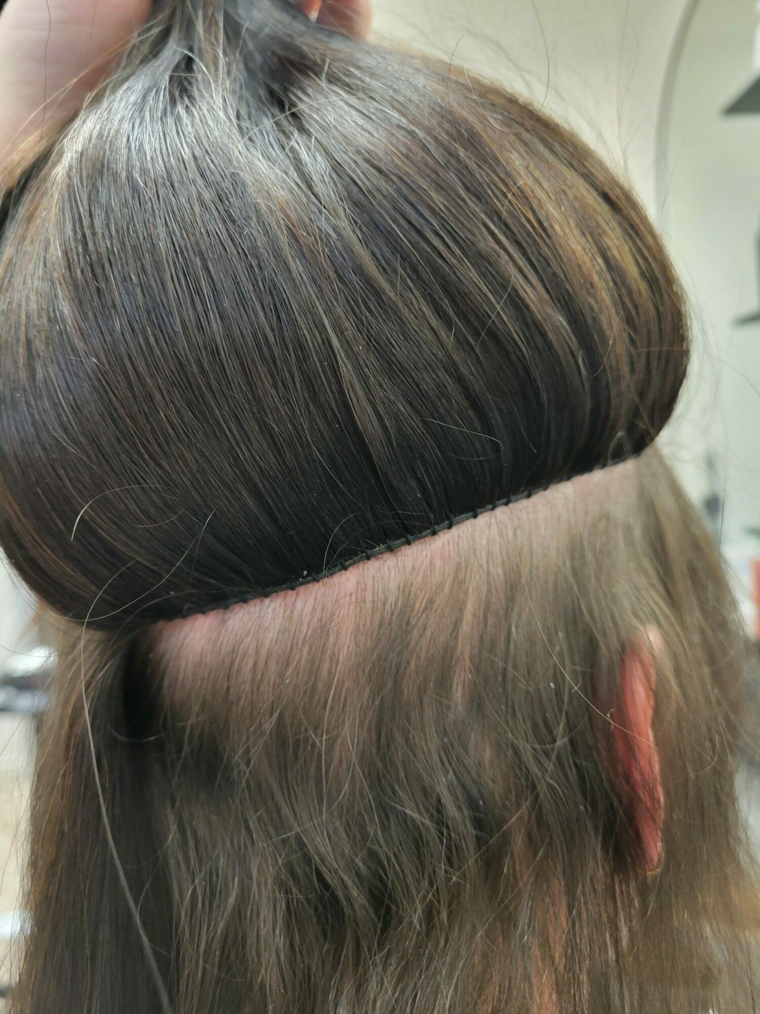 Close-up of a person's head showing hair being parted, with hair pulled back and a section of scalp visible.
