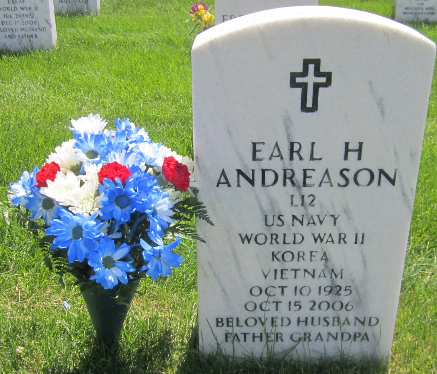Gravestone with a cross, inscribed with Earl H. Andreason's name, military service, and dates, beside a bouquet of blue, white, and red flowers.