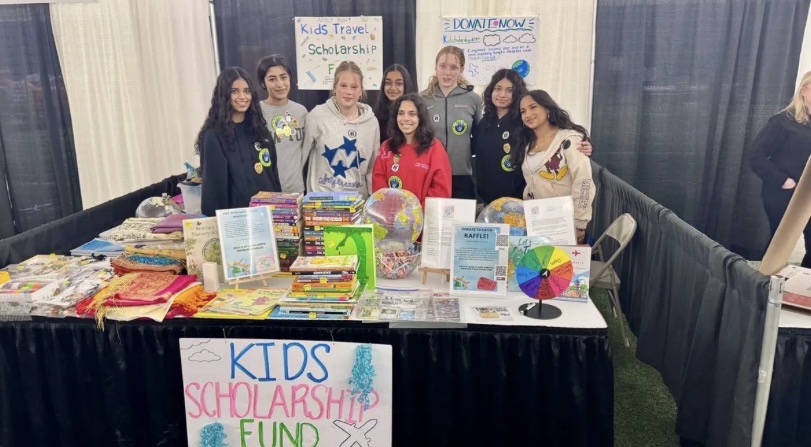 Group of children standing behind a table with colorful items and signs at a school event.