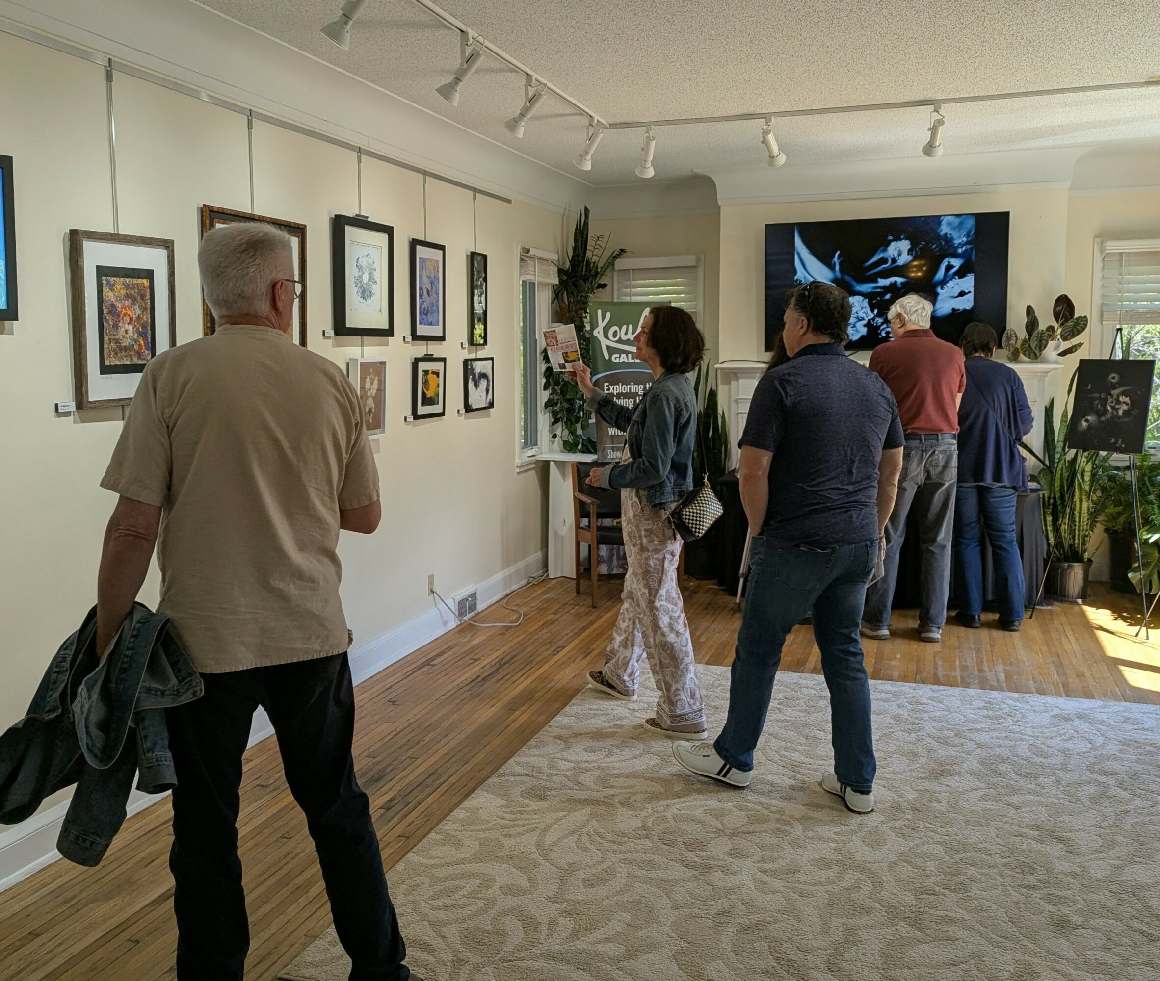 People viewing artwork and a large screen in an art gallery with framed pictures on the wall.