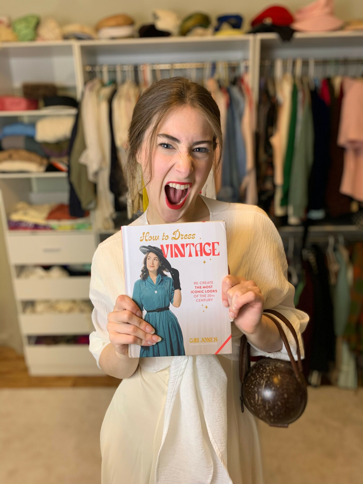 Young woman with light brown hair holding a magazine, winking and sticking out her tongue, in a clothing store.