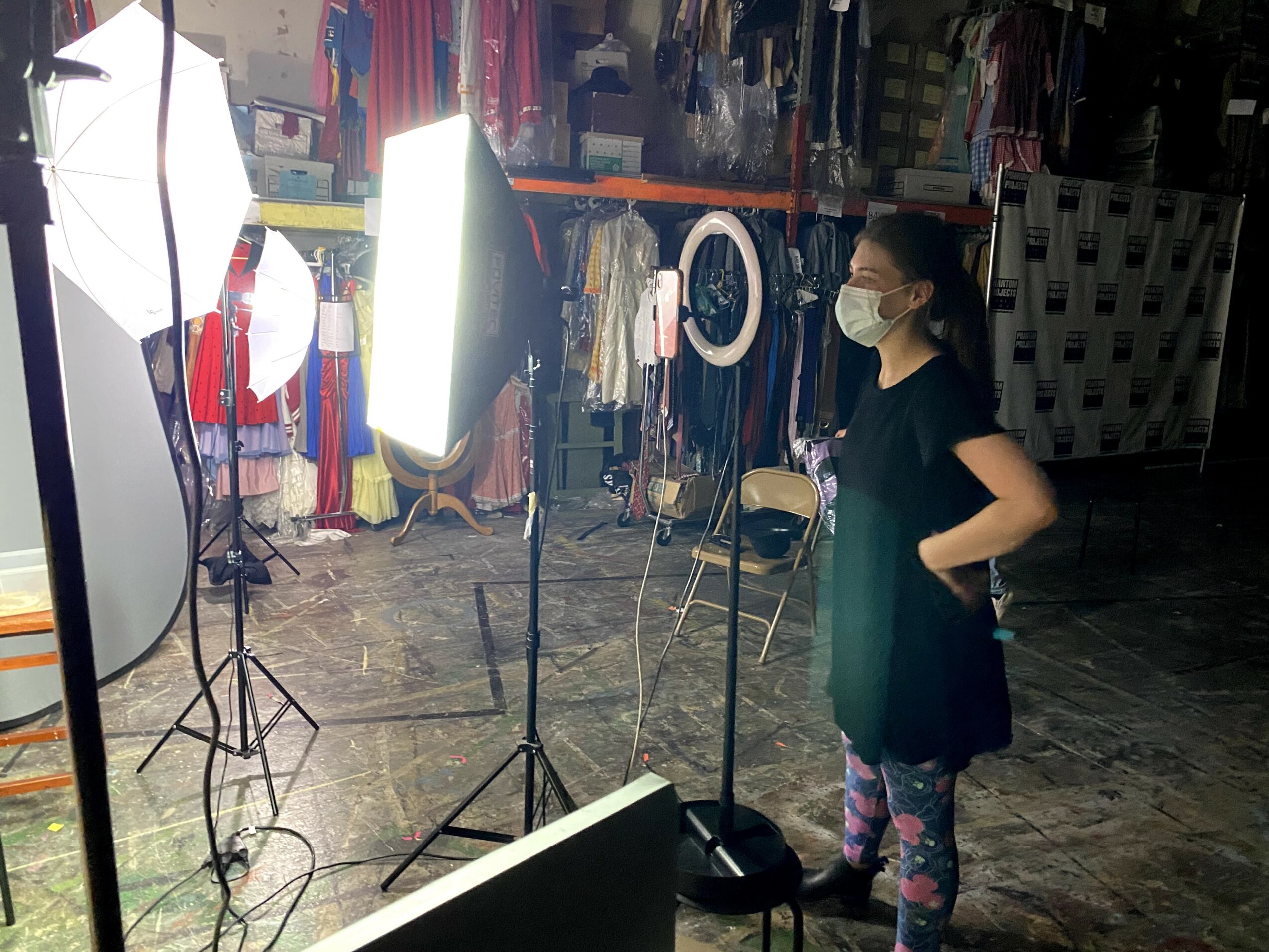 A girl wearing a face mask stands in front of a bright light in a store, with clothing hanging in the background.