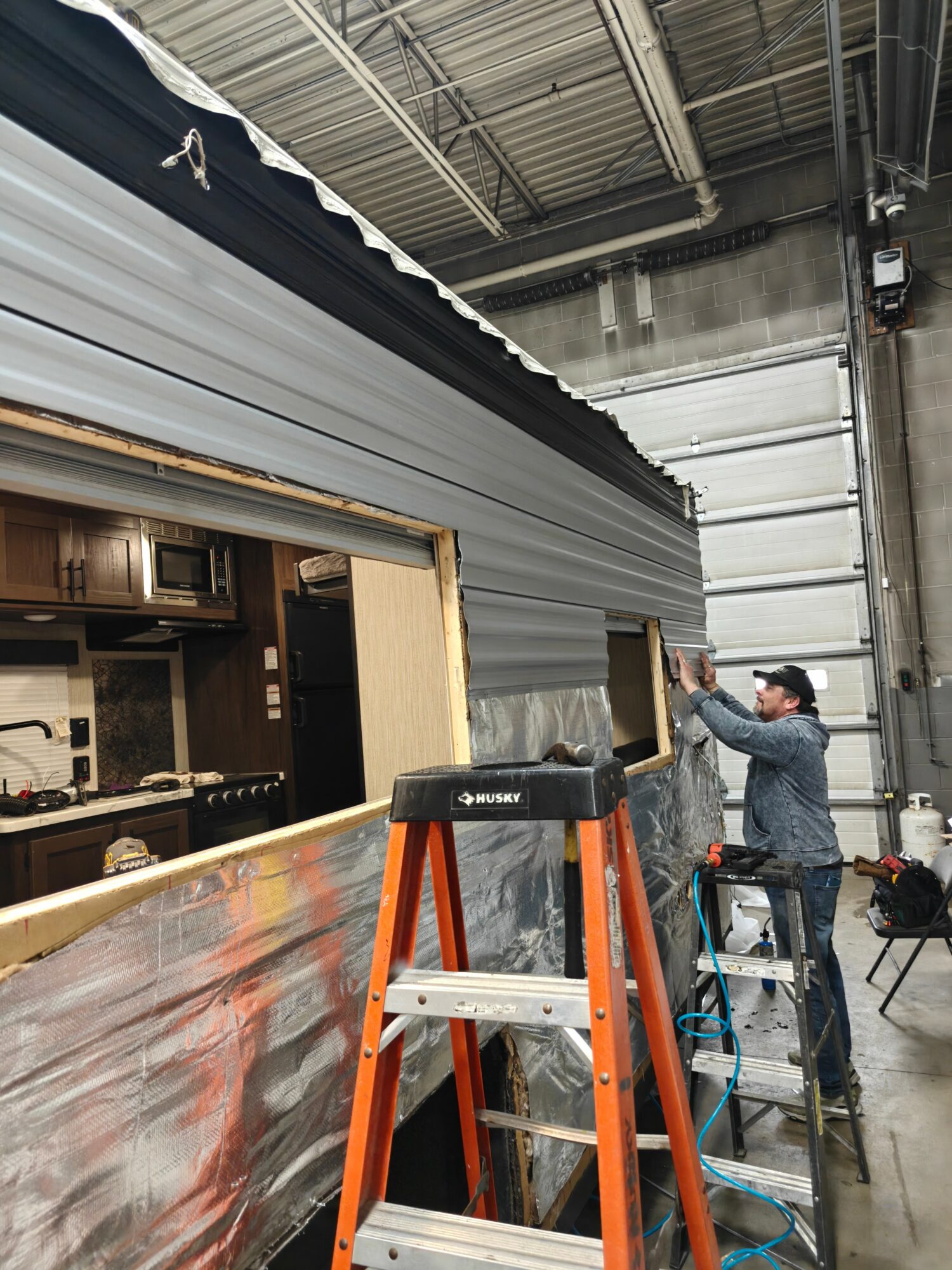 Person installing or repairing siding on a building with a ladder inside a warehouse or industrial space.