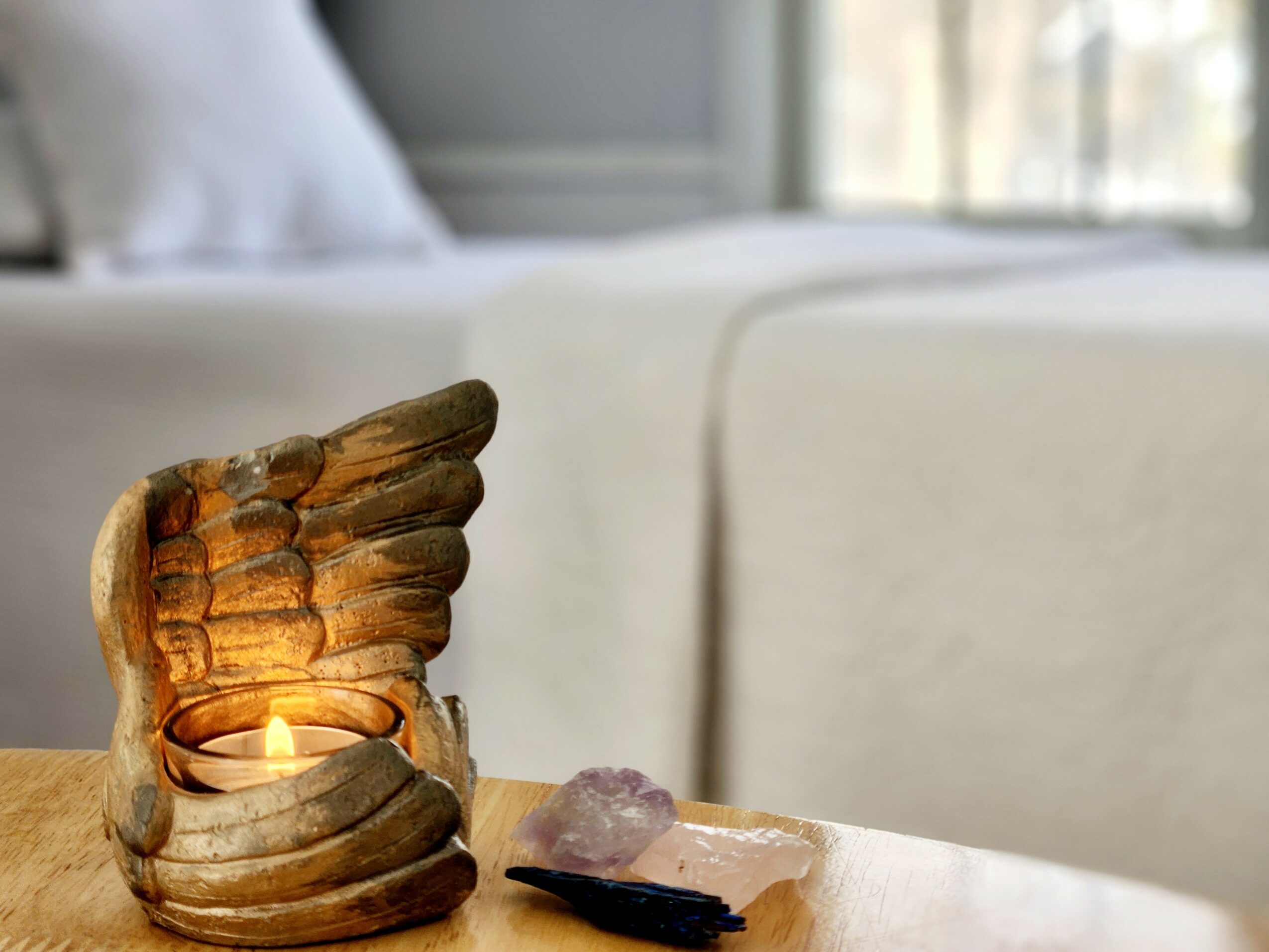 A wooden sculpture with a lit candle inside, placed on a table near a window with a sofa in the background.