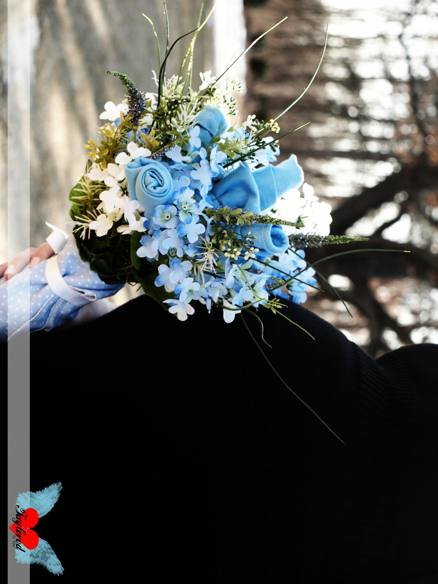 Person holding a bouquet of blue and white flowers outdoors, with trees in the background.
