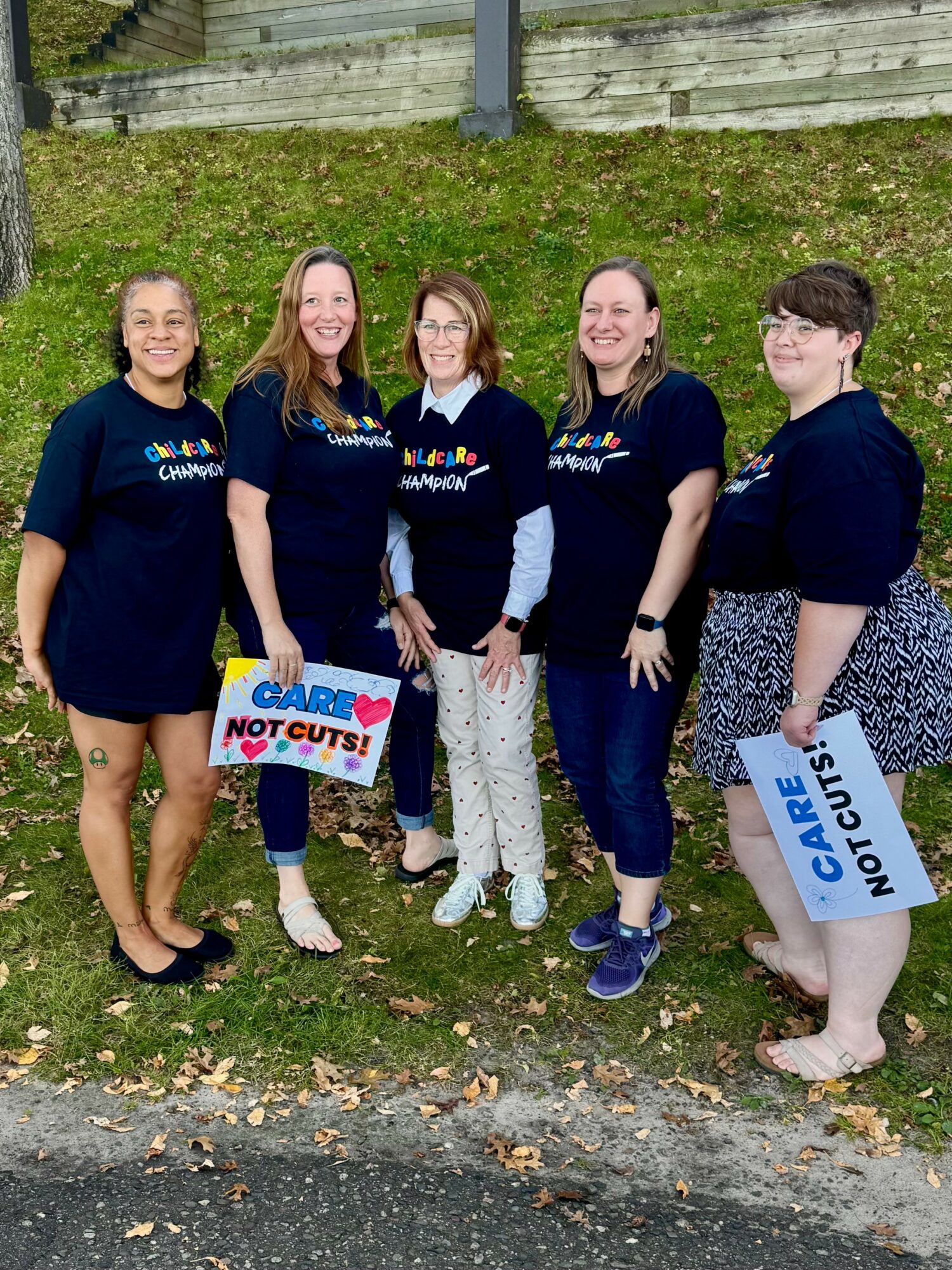Five people standing outdoors on grass, holding a sign that says 